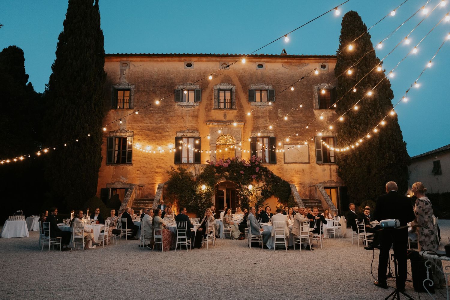 Outdoor wedding venue at dusk with string lights and rustic Italian architecture.