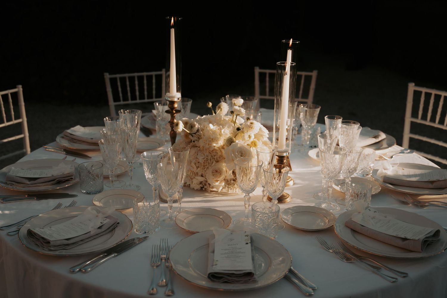 Candlelit wedding reception tables decorated in white with elegant place settings and centerpieces.
