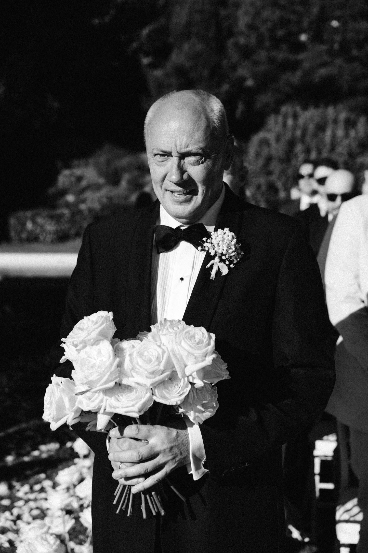 White roses in wedding bouquets are held during an outdoor ceremony.
