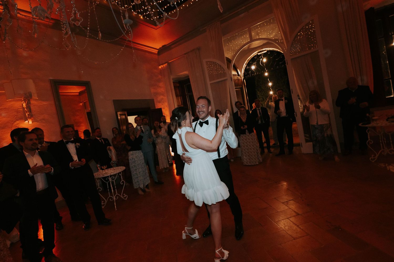 Wedding reception dance floor bathed in warm red lighting with guests celebrating.