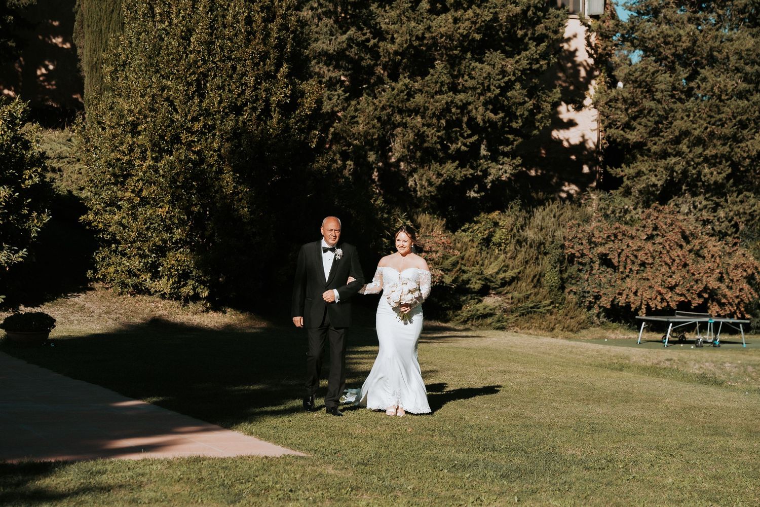 Wide landscape shots of a wedding ceremony setup on a grassy hillside surrounded by trees.