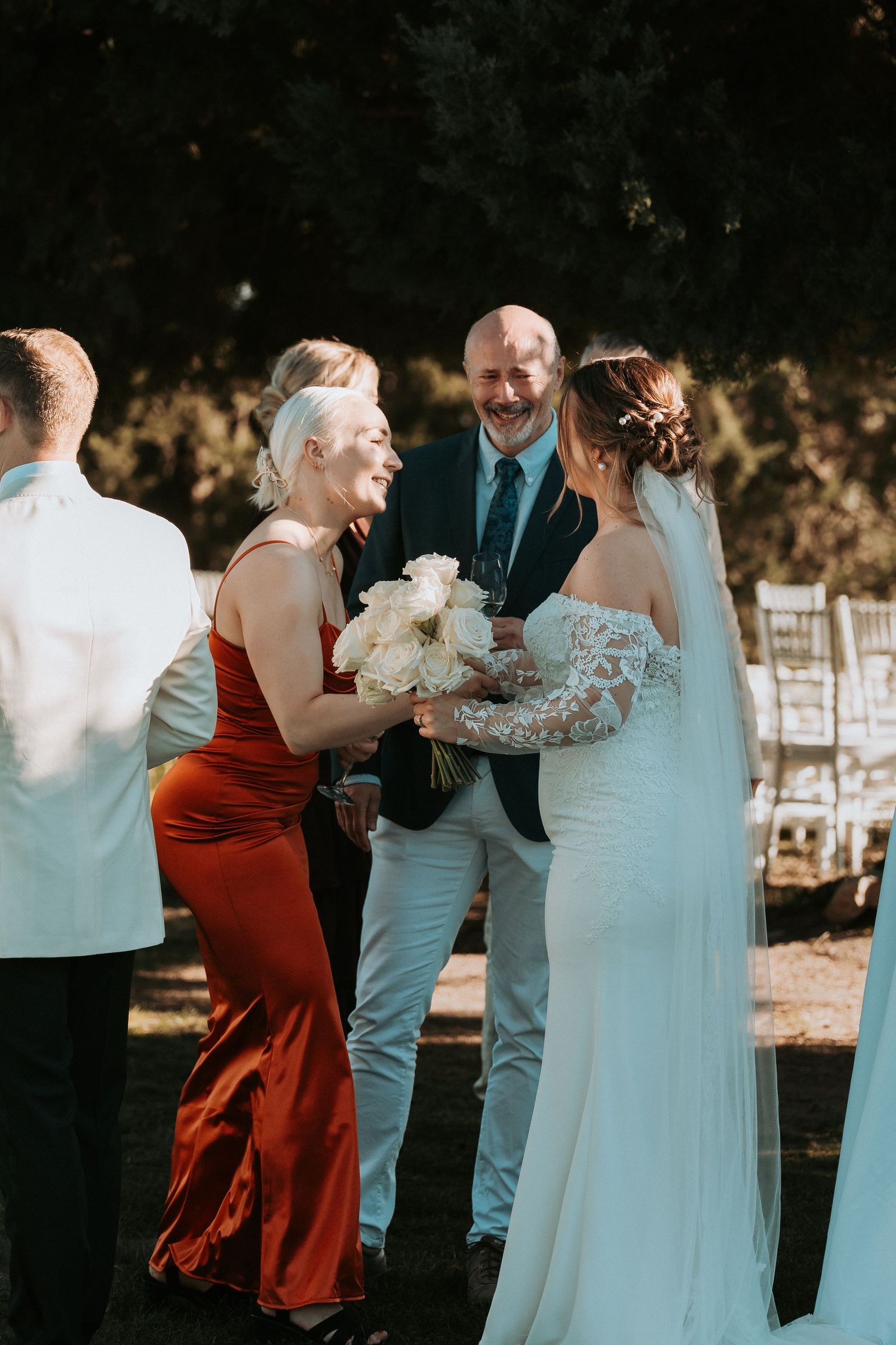 Wedding party in formal attire gathered outdoors with bridesmaids in burgundy dresses.