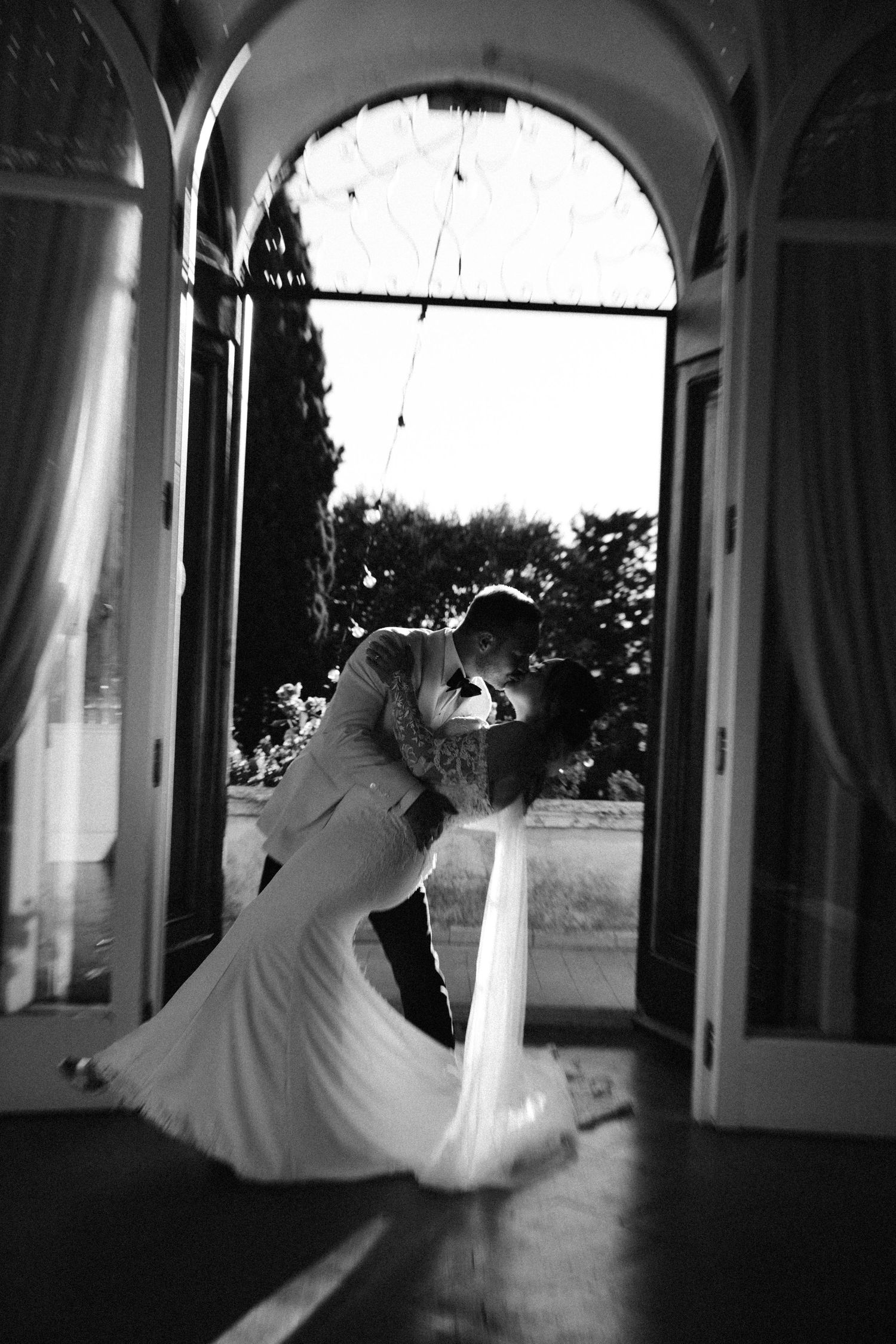 Dramatic black and white photo of newlyweds dancing in an arched doorway.
