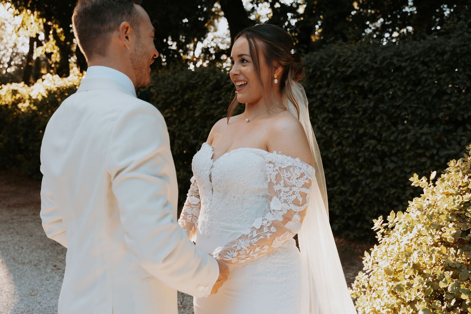 Elegant couple in white wedding attire sharing a tender moment in golden sunlight.