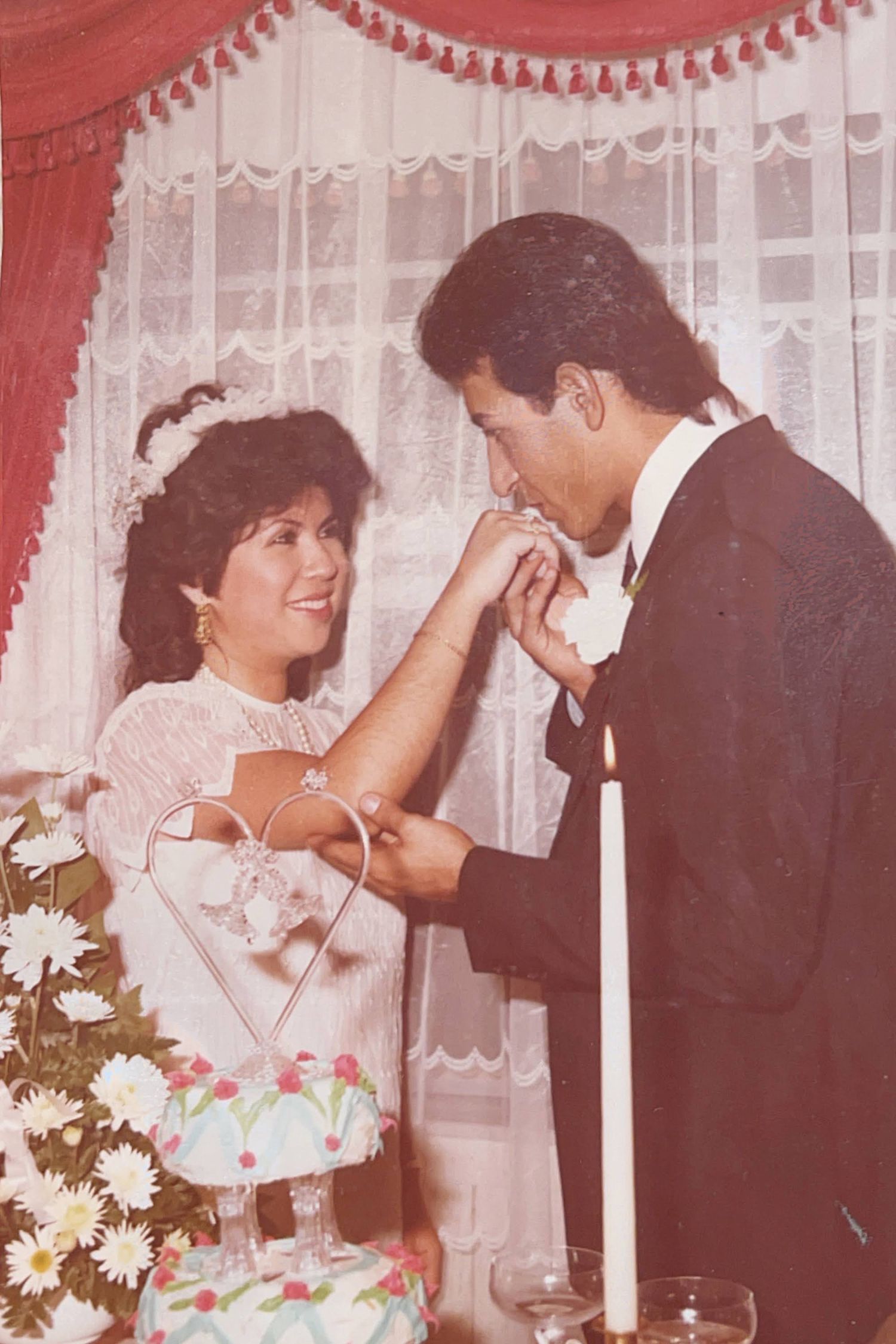 Vintage wedding photo showing a tender moment between newlyweds with white curtains and flowers.