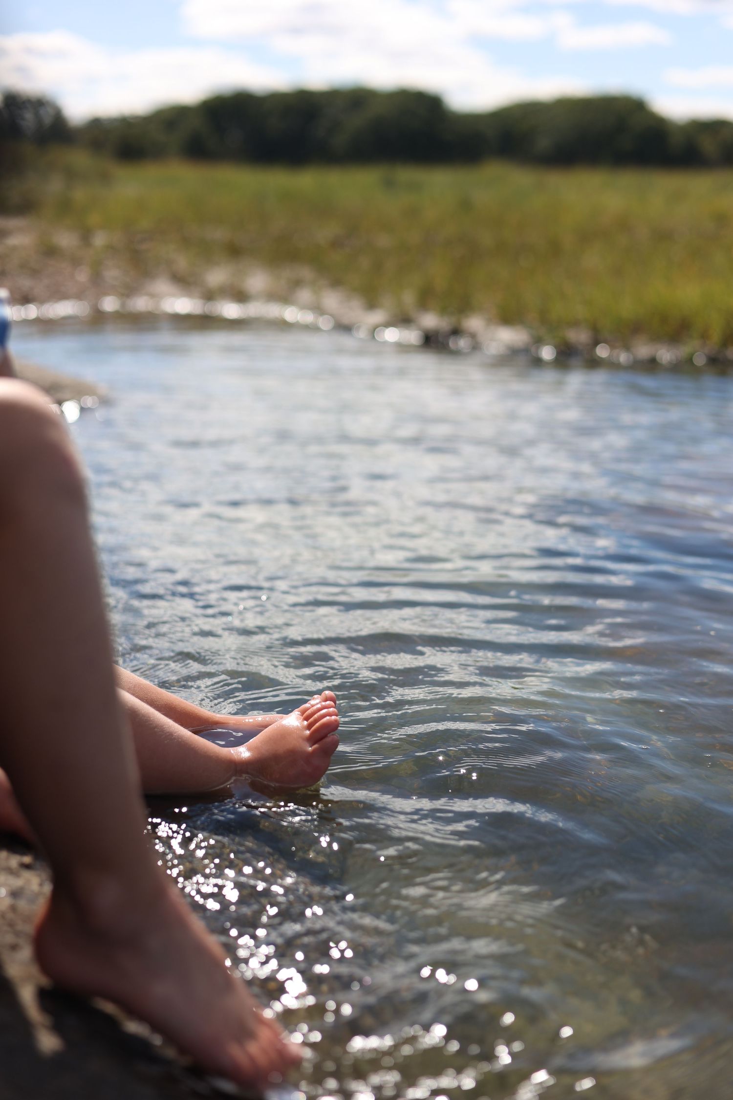 Feet dangling in sparkling lake water on a sunny summer day creating ripples on the surface. north shore massachusetts
