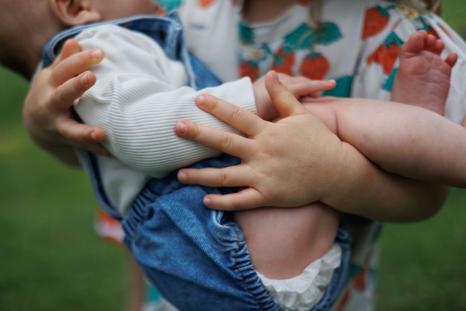 Baby wearing blue overalls and white socks being held by adult hands in a series of photos. north shore massachusetts