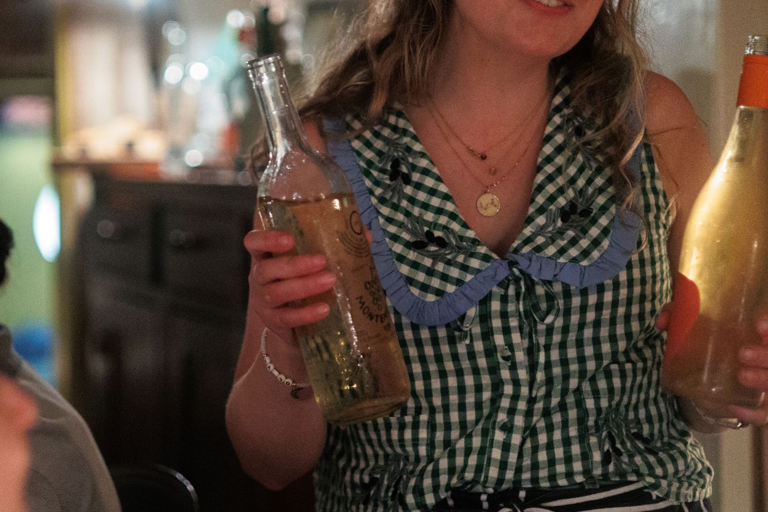 A person in a black and white gingham shirt holds various drinks and poses in a dimly lit setting. north shore massachusetts