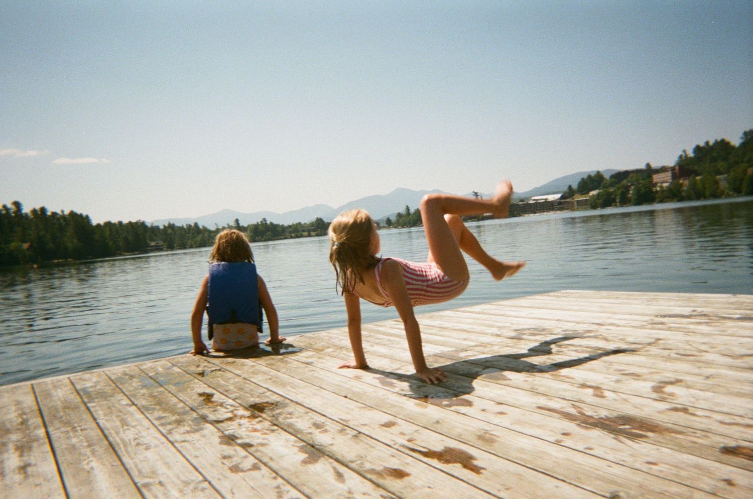 People relaxing on a wooden dock by a serene lake during summer with mountains in the background. lake placid ny