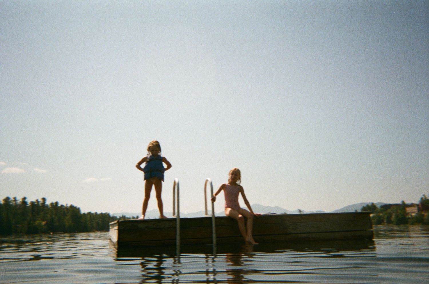 Silhouettes of people standing on a wooden dock overlooking a serene lake during sunset. lake placid ny