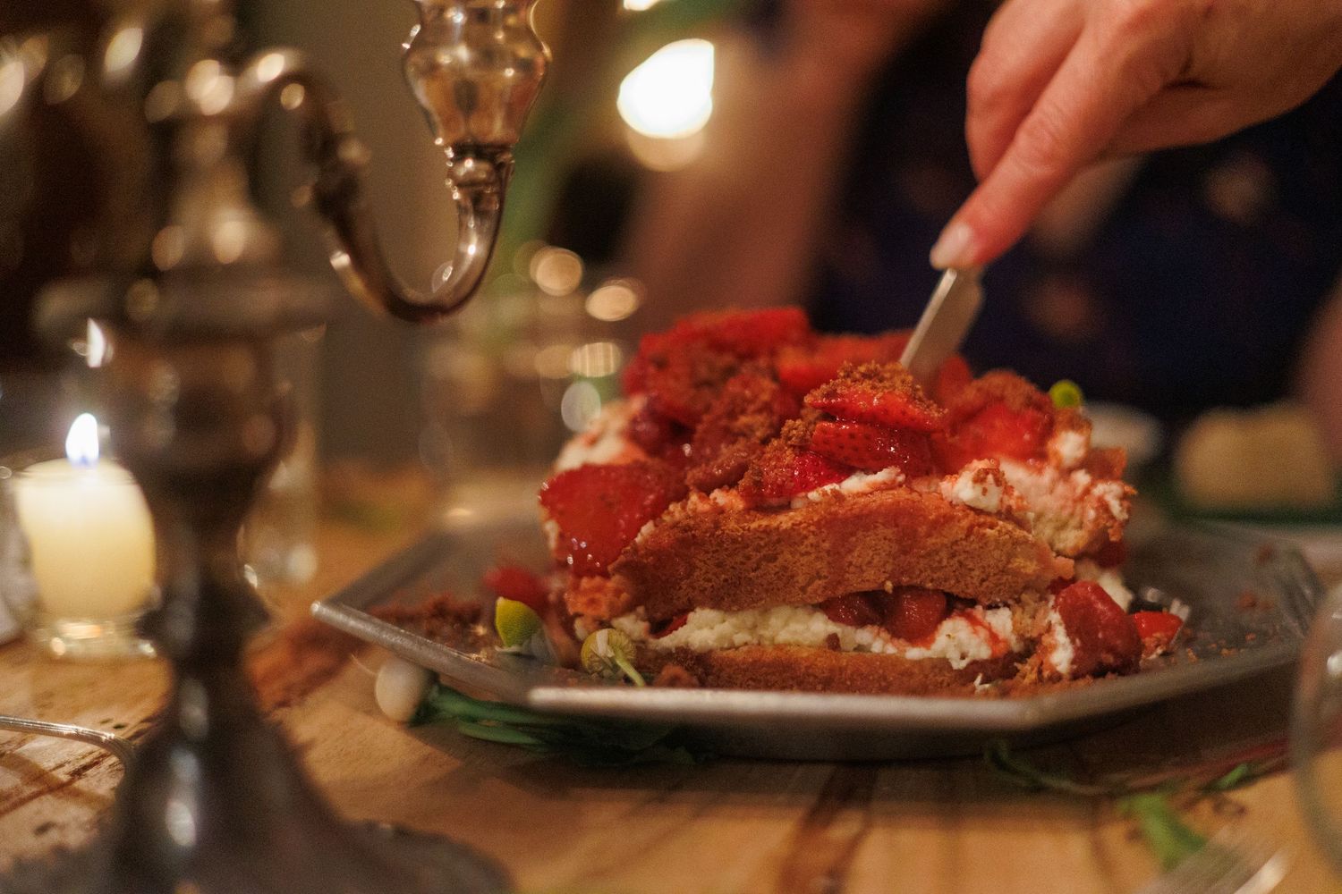 A close-up shot of hands serving an elegant plated strawberry dessert at a candlelit dinner table. north shore massachusetts