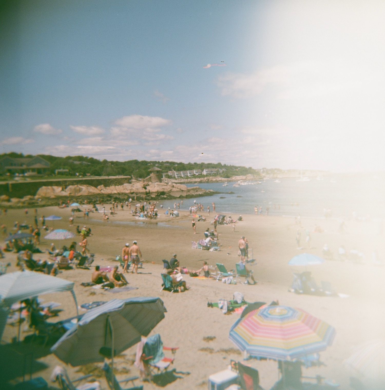 A panoramic view of a sandy beach on a sunny day with scattered umbrellas and beachgoers enjoying the coastline. rockport massachusetts