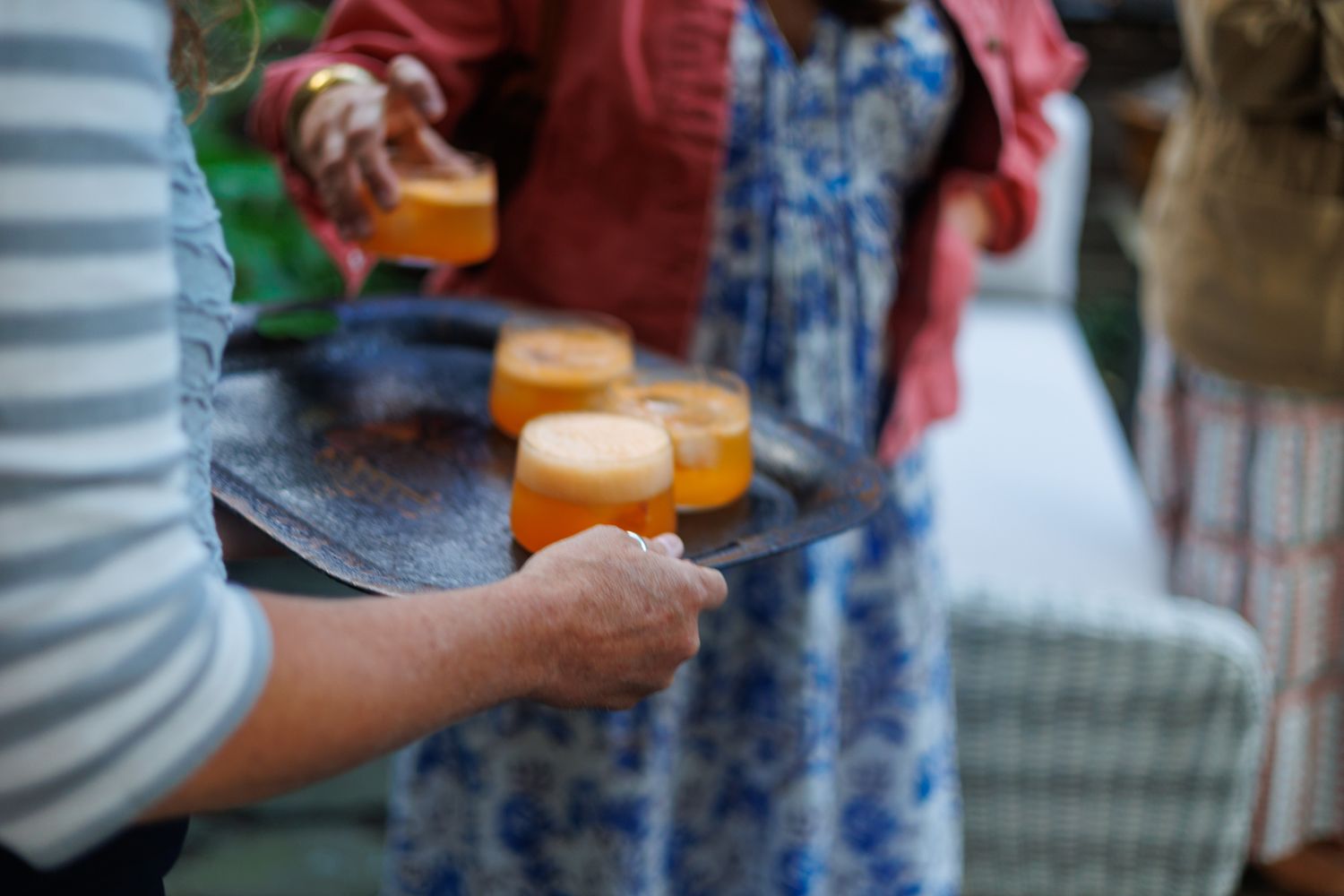 Person in a striped shirt and floral pants holding cocktails, summer outdoor party, north shore massachusetts