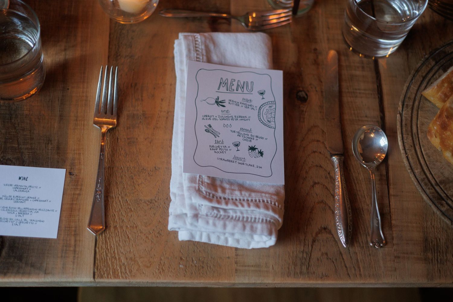 Place settings with silverware and glasses arranged on a rustic wooden table with menu cards and notes. north shore massachusetts