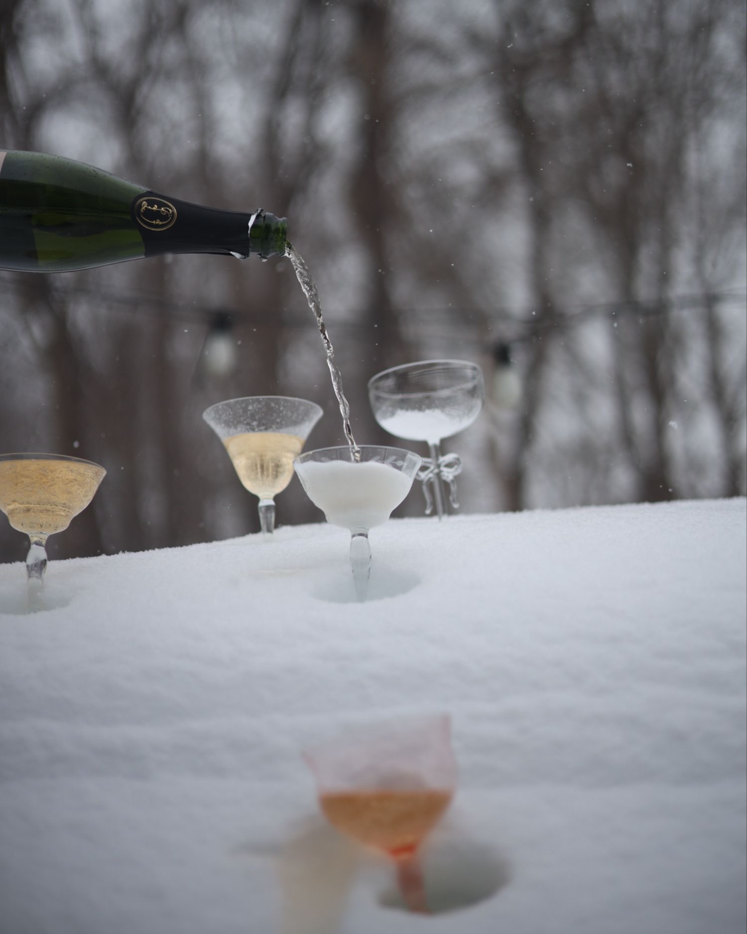 Champagne being poured into elegant glasses arranged in snow during winter, creating a festive outdoor scene. north shore massachusetts