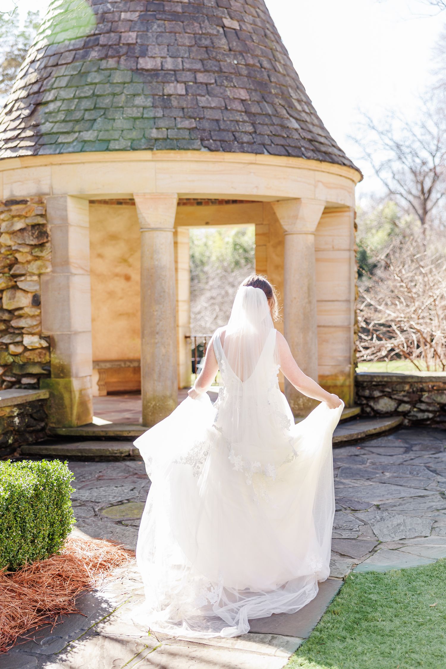 White wedding dress flowing in the breeze against stone gazebo architecture at the Graylyn Estate with Winston Salem Wedding photographer
