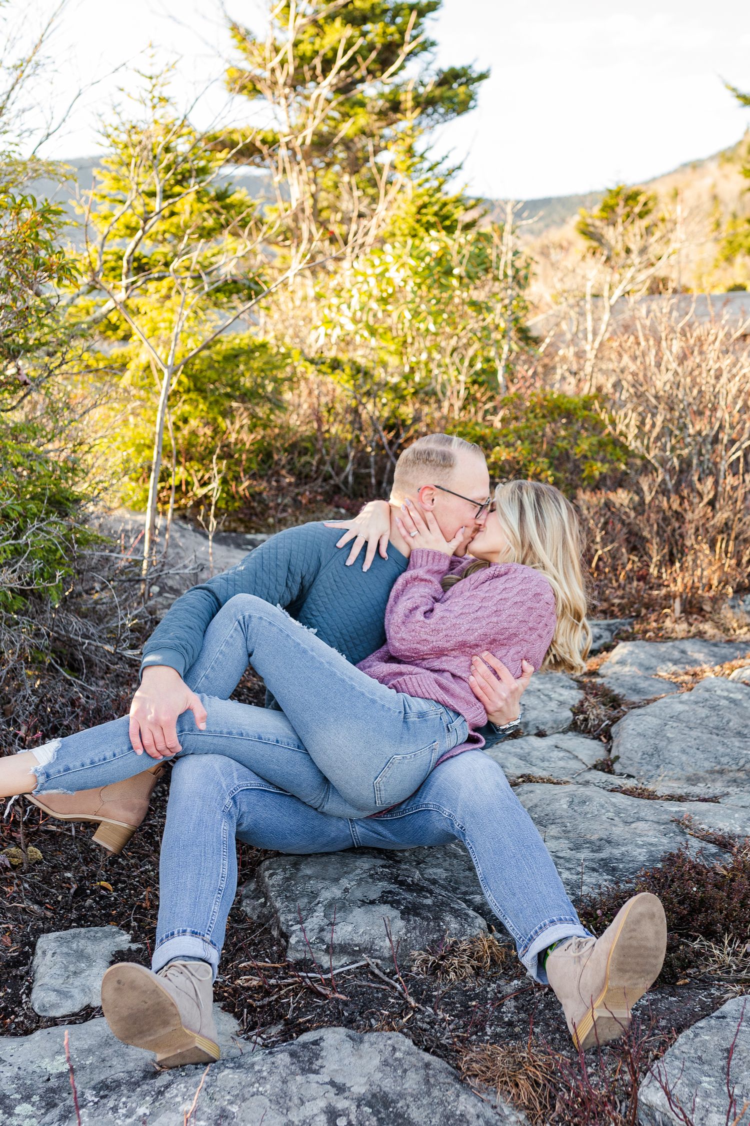 Couple lounging together on rocky mountain overlook during sunset wearing casual sweaters and jeans Boone NC Engagement Photographer on the