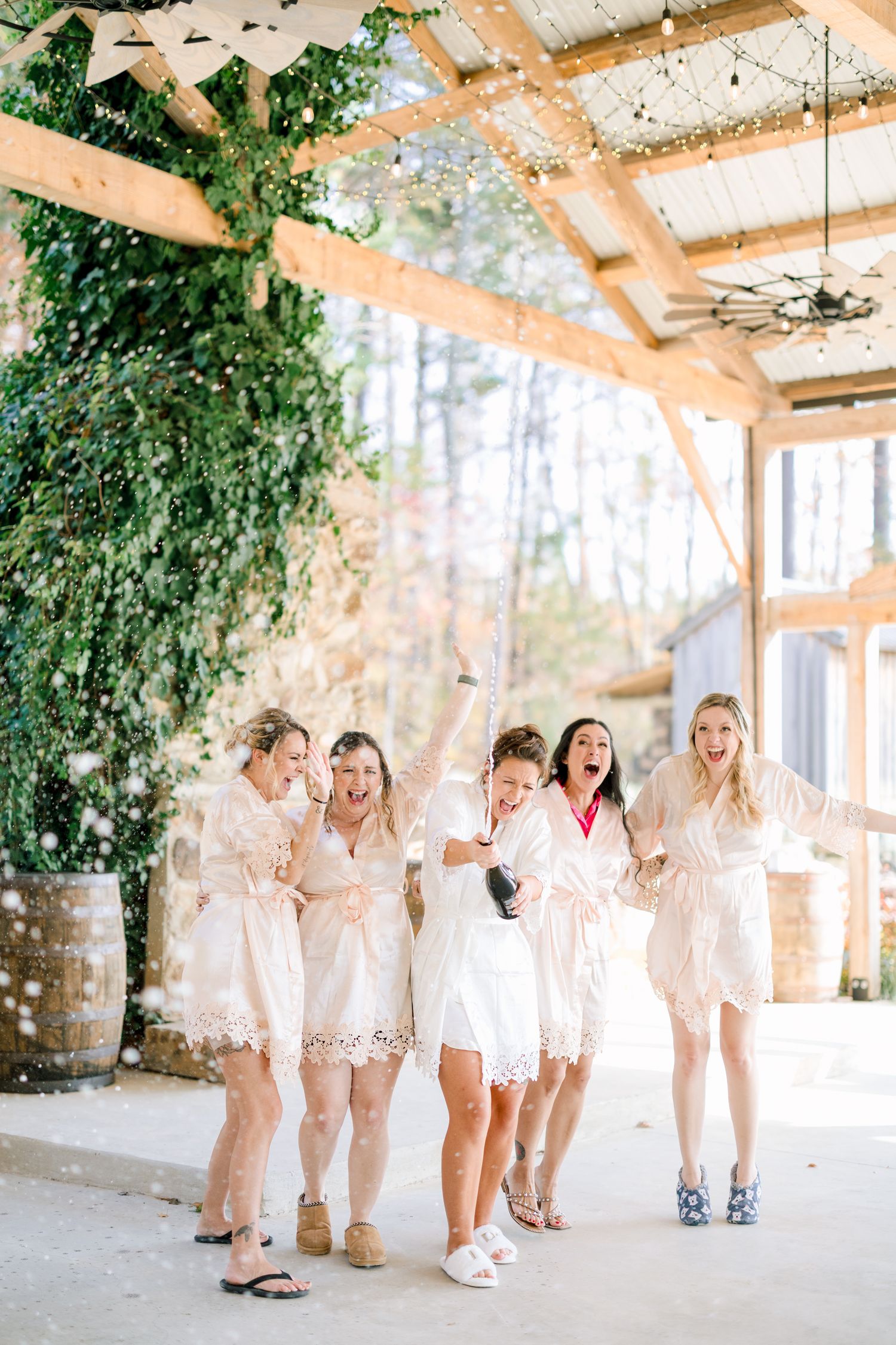 Wedding party in all-white outfits poses under rustic wooden pergola with greenery at the Barn at Union Grove Farm in Chapel Hill