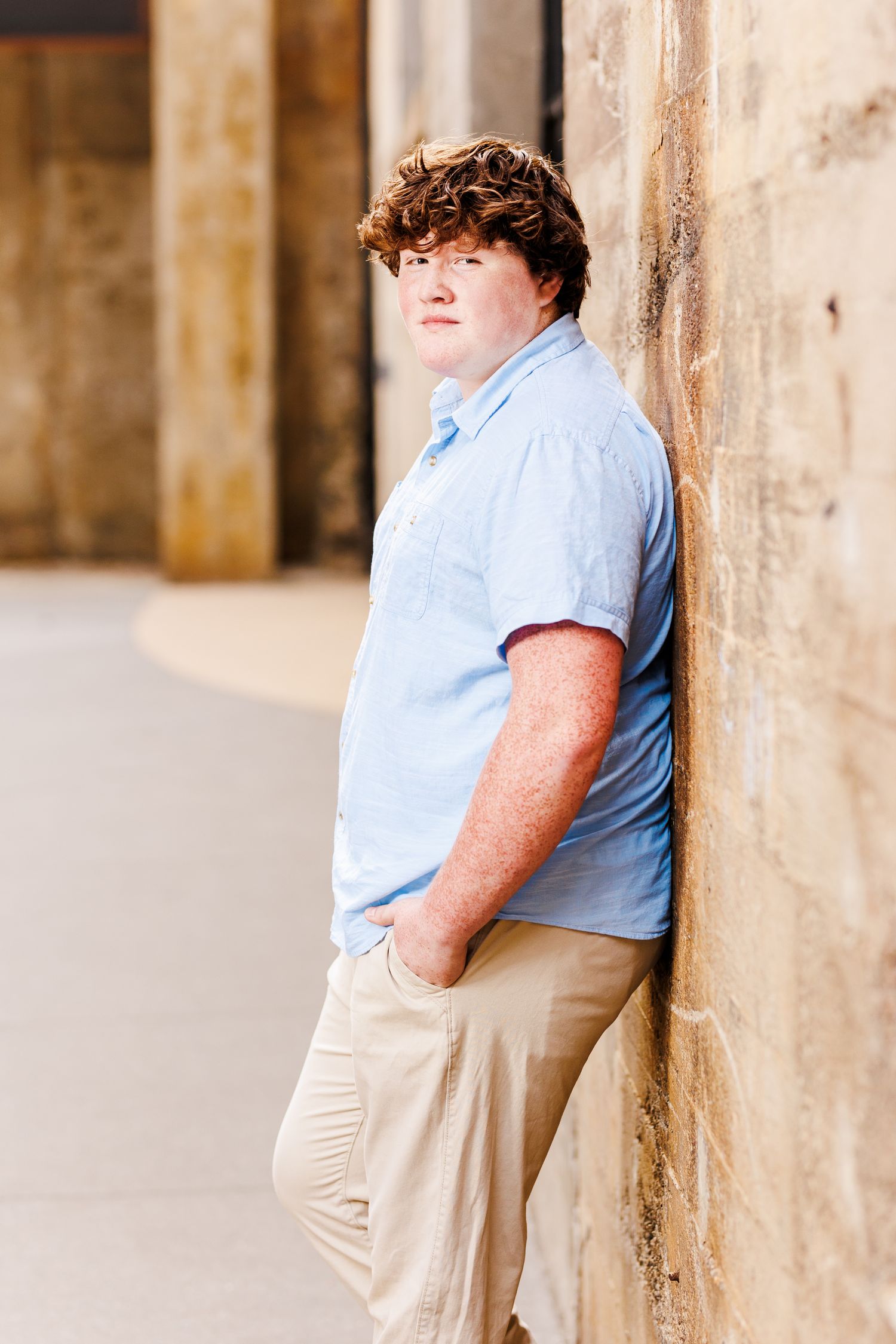 Portrait series against stone wall in casual light blue shirt and khaki pants  for Senior Portrait Session in Winston Salem