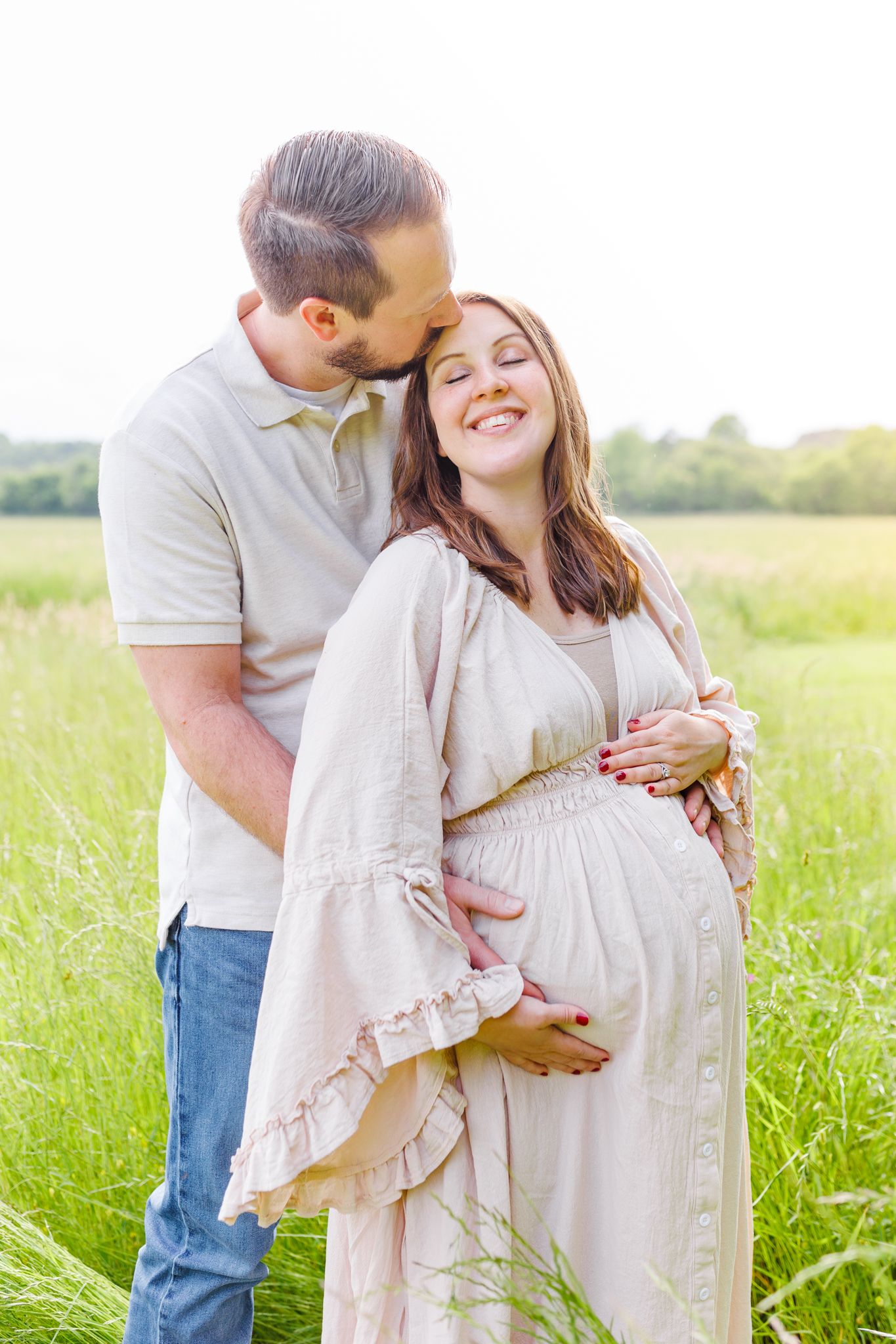 Romantic maternity photos in a sunlit meadow with couple embracing.