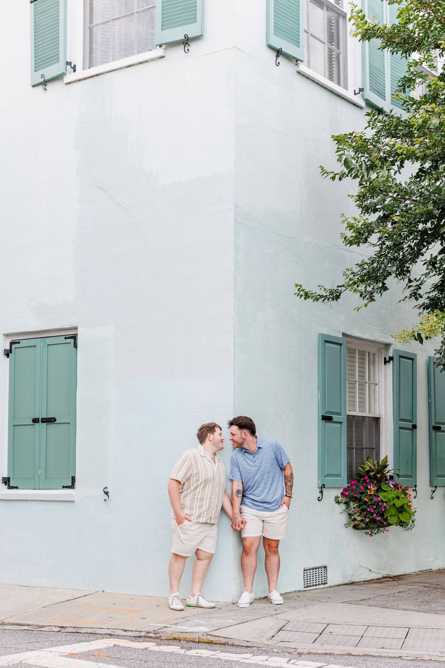 Couple strolling along white buildings with mint green shutters in historic Charleston with Charleston Engagement Photographer at Rainbow Ro
