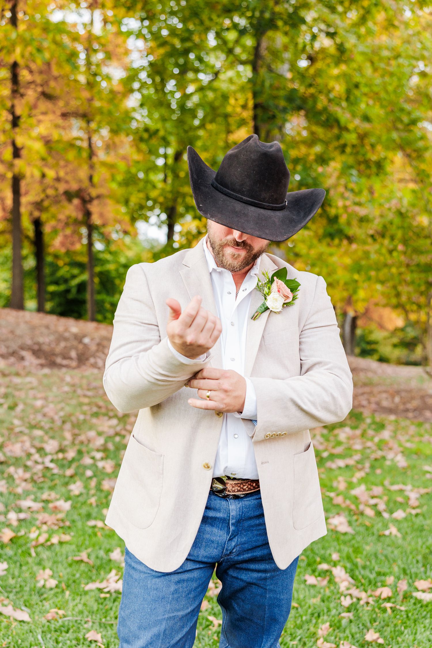 Person in white jacket and cowboy hat poses playfully in autumn setting with fallen leaves at the Winmock with NC Wedding Photographer