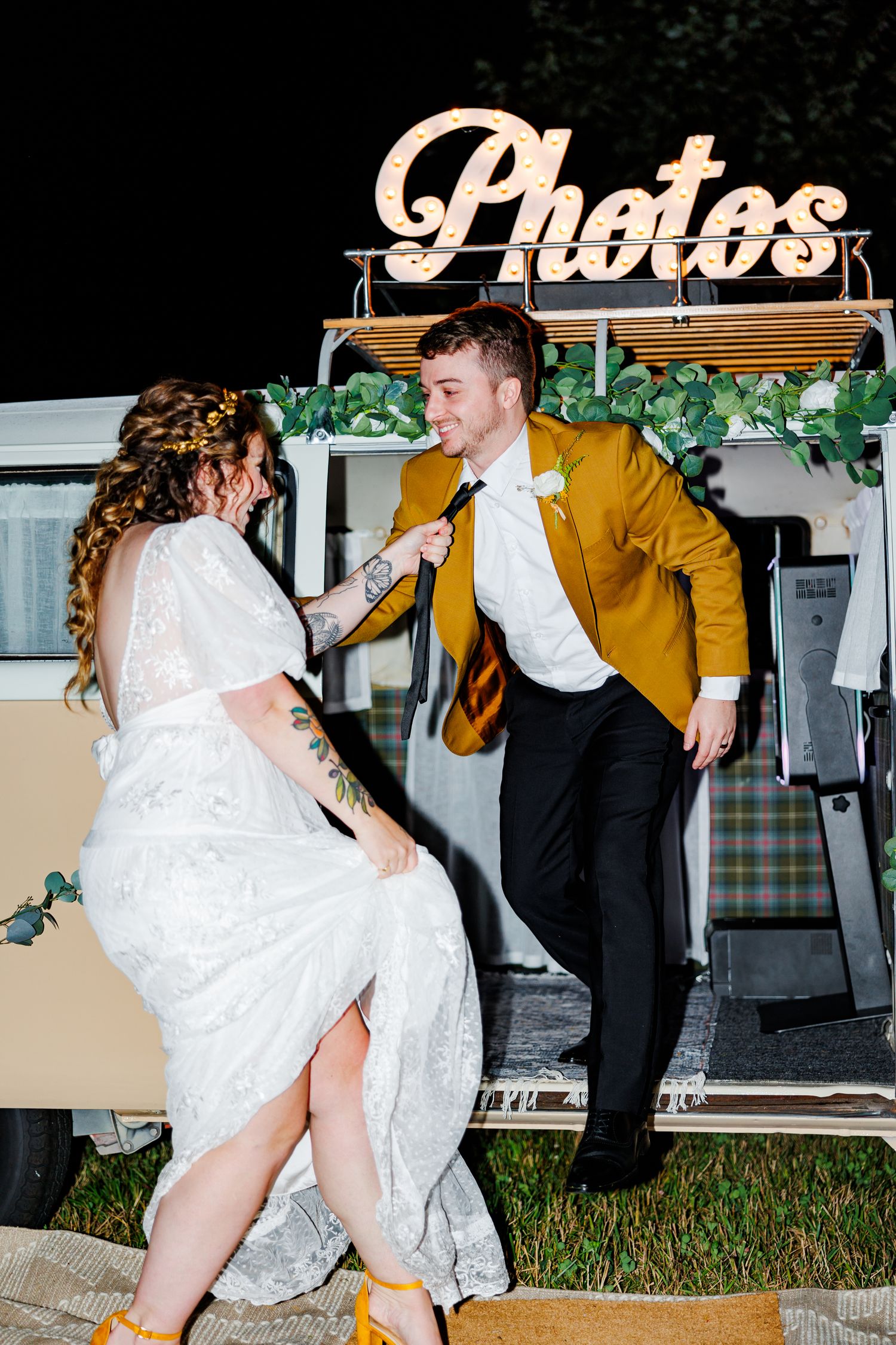 Playful wedding couple dancing and posing in front of a photo booth sign.