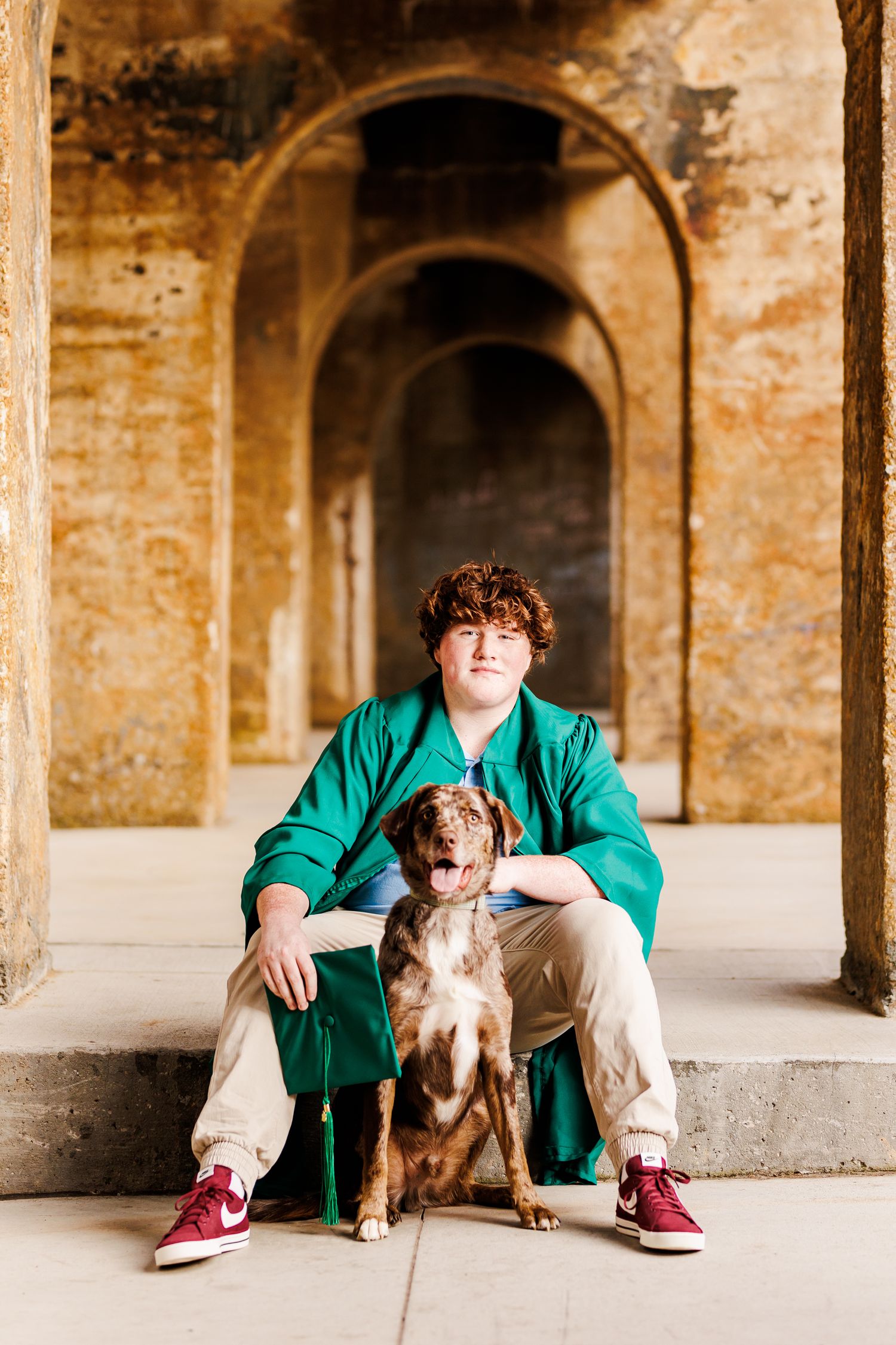 Casual portraits with a dog under historic stone archways in green attire  for Senior Portrait Session in Winston Salem