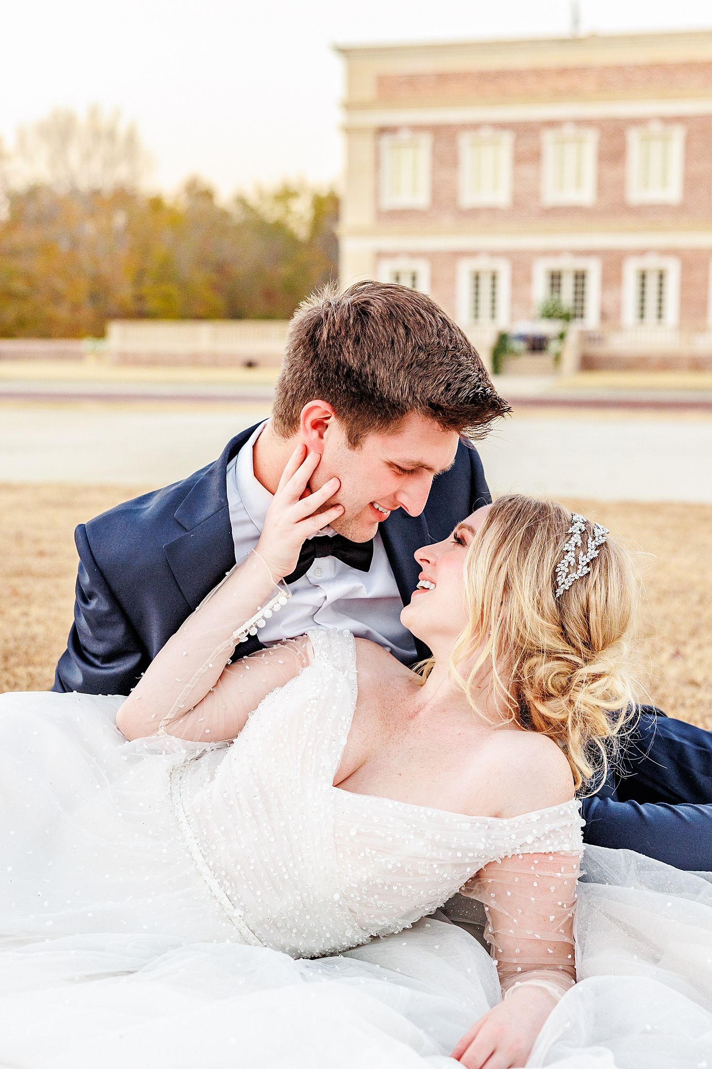 Romantic wedding couple lying on grass in front of a historic pink building with Raleigh Wedding Photographer