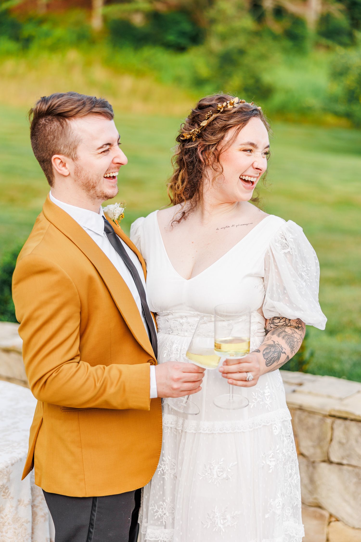 Couple in wedding attire sharing drinks and laughter outdoors at the Barn at New River with NC Wedding Photographer
