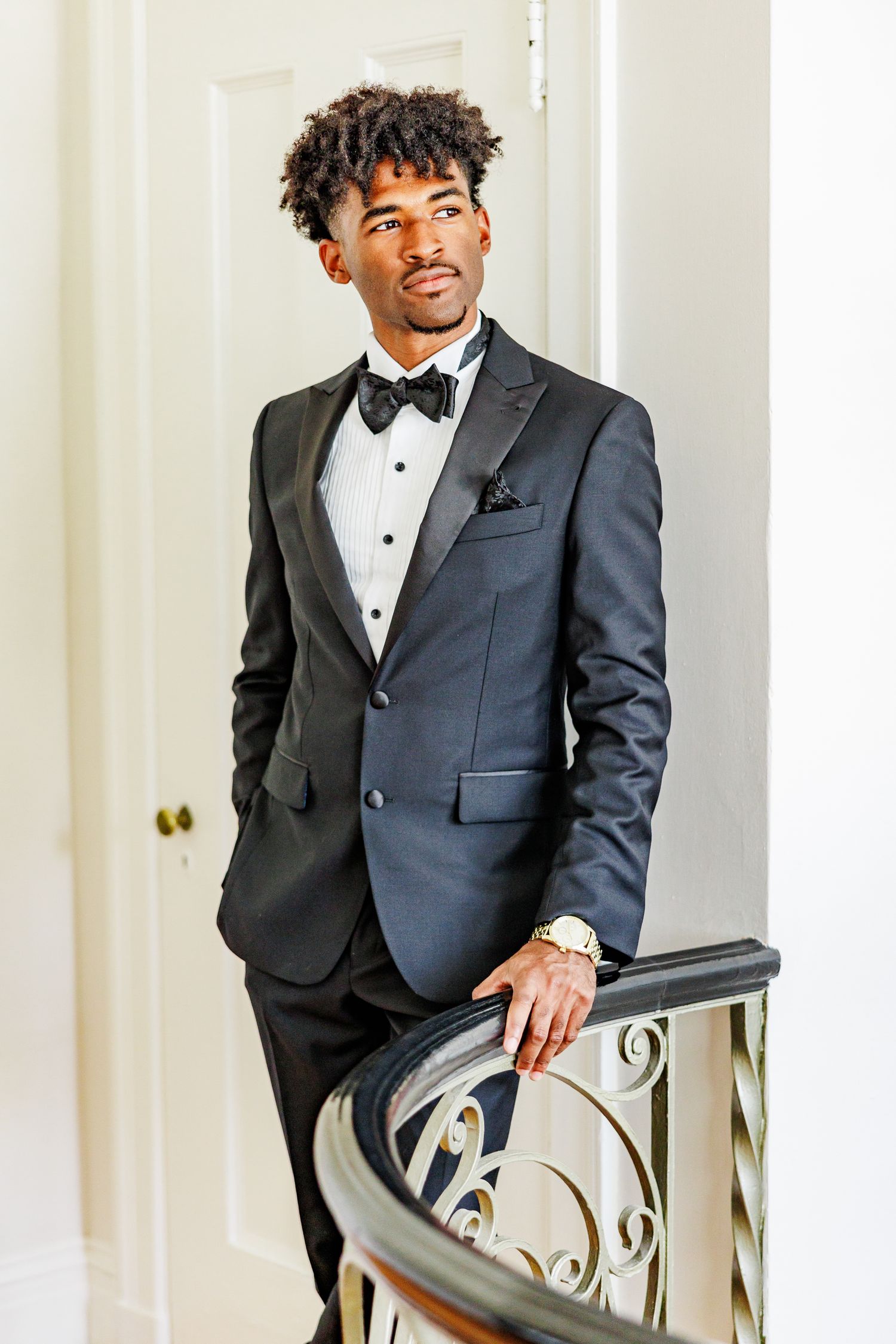 Groom in formal black tuxedo posing elegantly against white backdrop with NC Wedding Photographer
