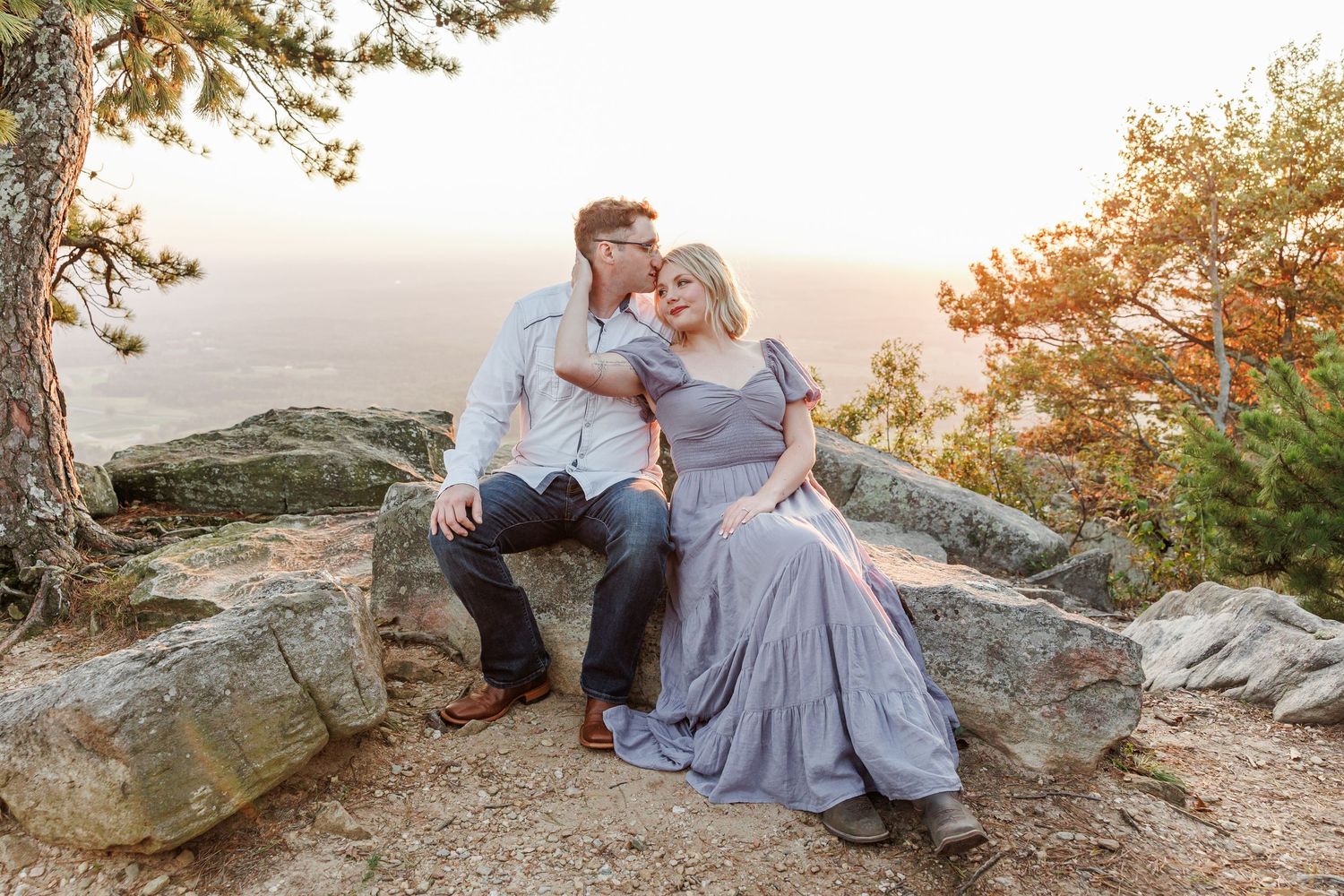A couple shares an intimate moment on a rocky overlook at sunset with Winston Salem Engagement Photographer at Pilot Mountain