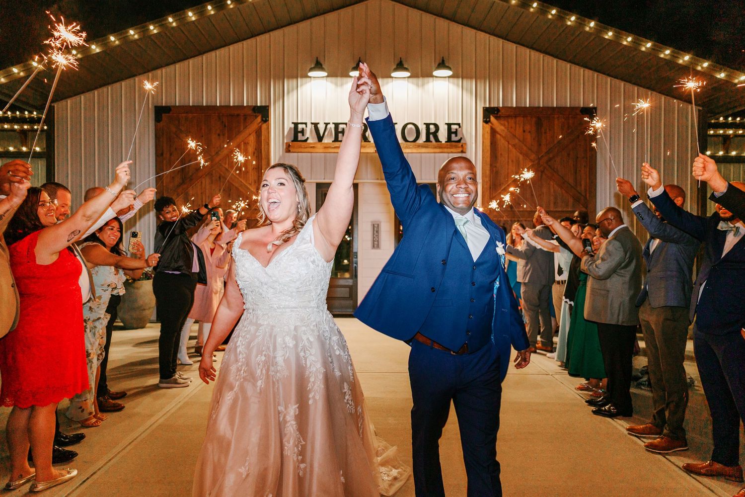 Newlyweds exit their barn wedding reception under sparklers held by cheering guests.