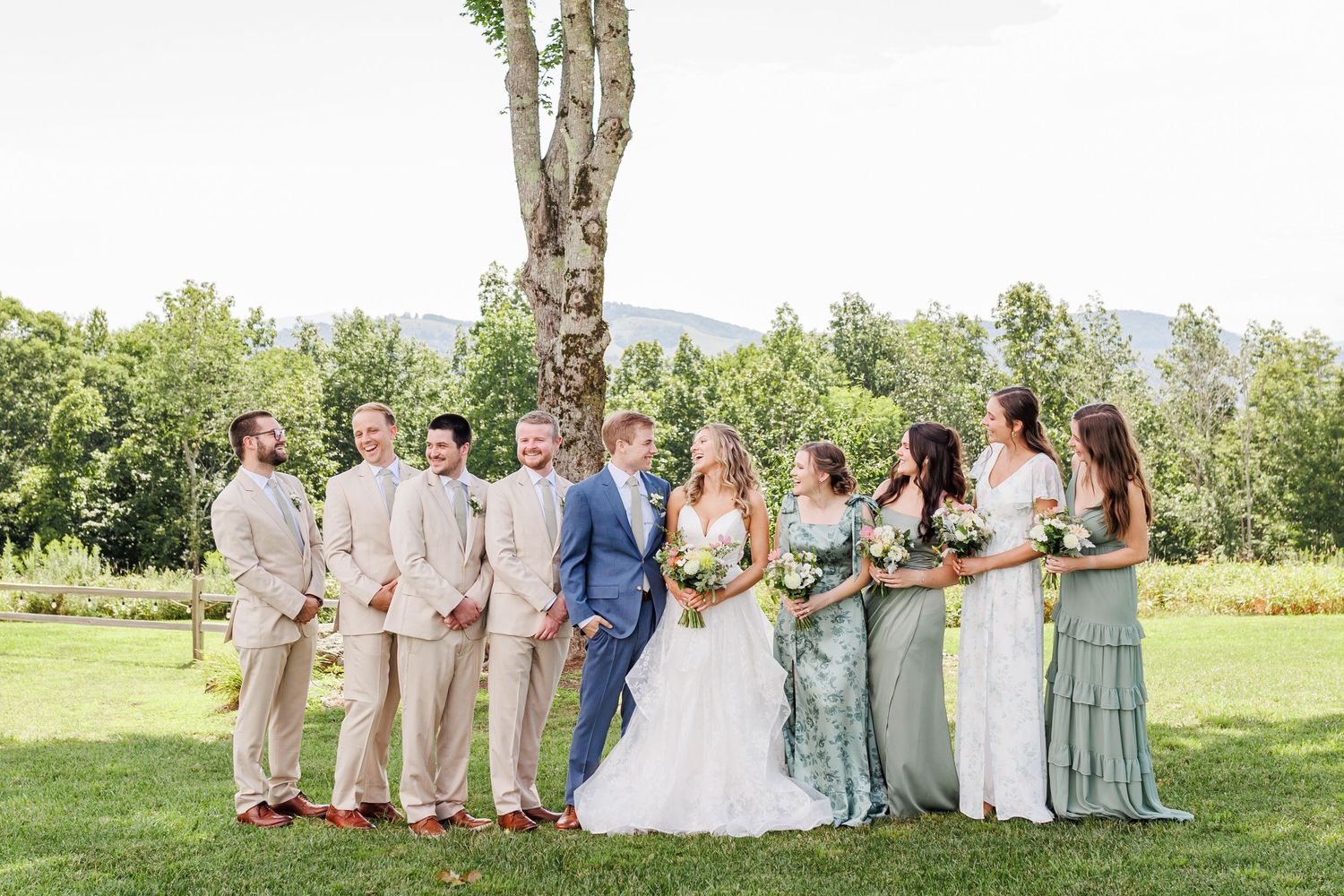 Wedding party in pastel dresses posed on green lawn with mountain backdrop at Appalachian View Venue with Boone Wedding Photographer