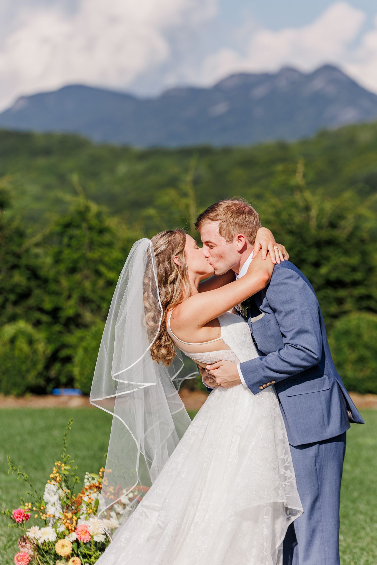 Romantic mountain wedding ceremony with couple embracing against scenic landscape.