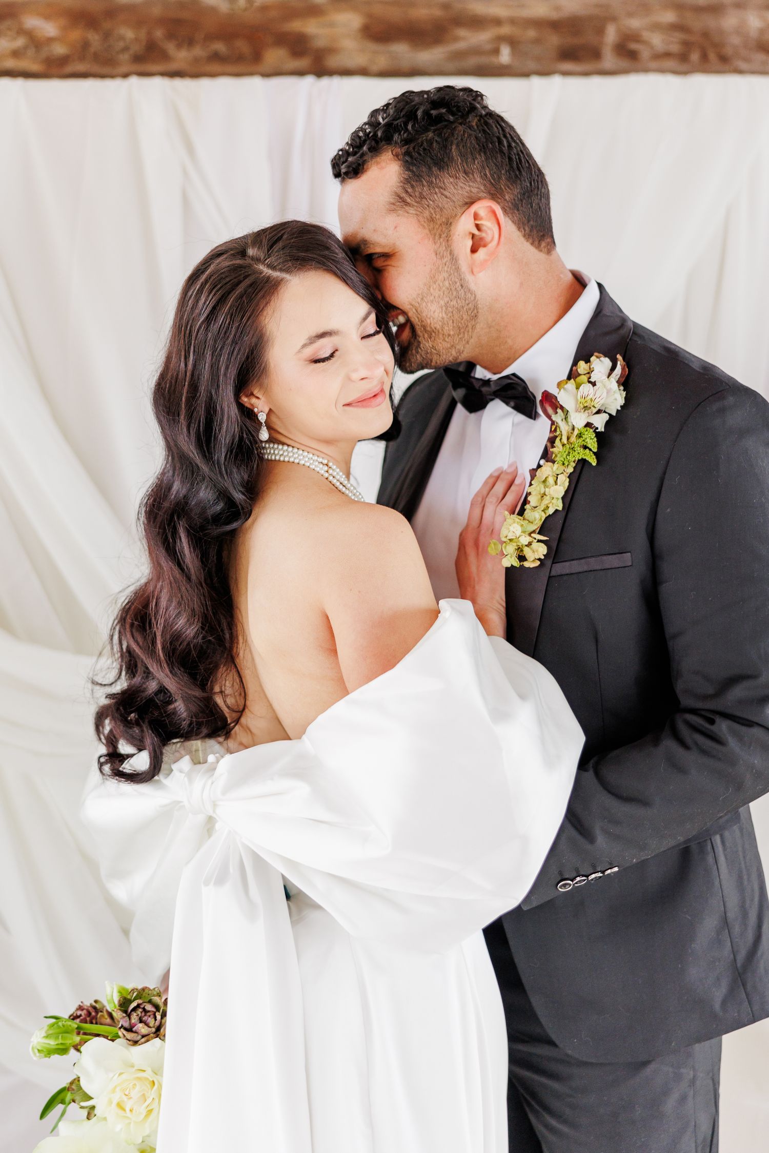 A romantic wedding couple embraces in front of a white backdrop with delicate floral details with Winston Salem Wedding photographer