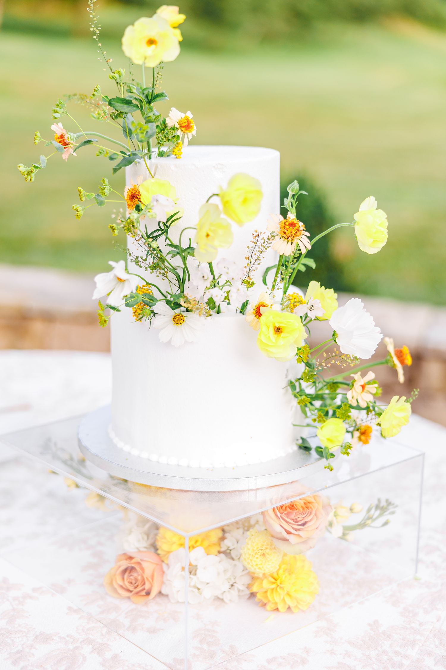 White wedding cake decorated with delicate yellow and peach flowers at the Barn at New River with NC Wedding Photographer