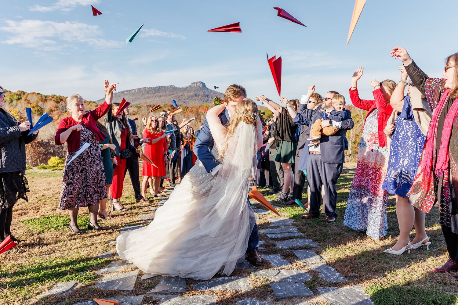 Wedding guests throw paper airplanes as newlyweds walk past during outdoor ceremony exit with North Carolina Wedding Photographer