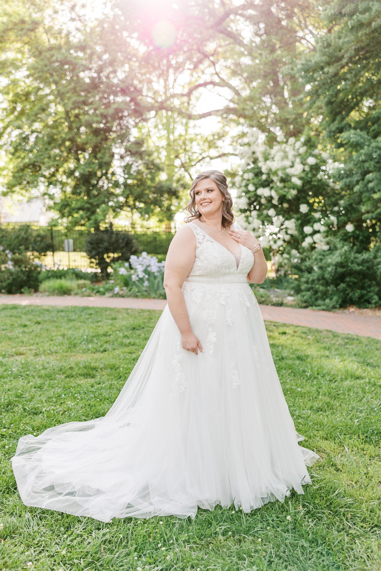 Beautiful white wedding gown with flowing train photographed in a sunlit garden setting with Winston Salem Wedding Photographer