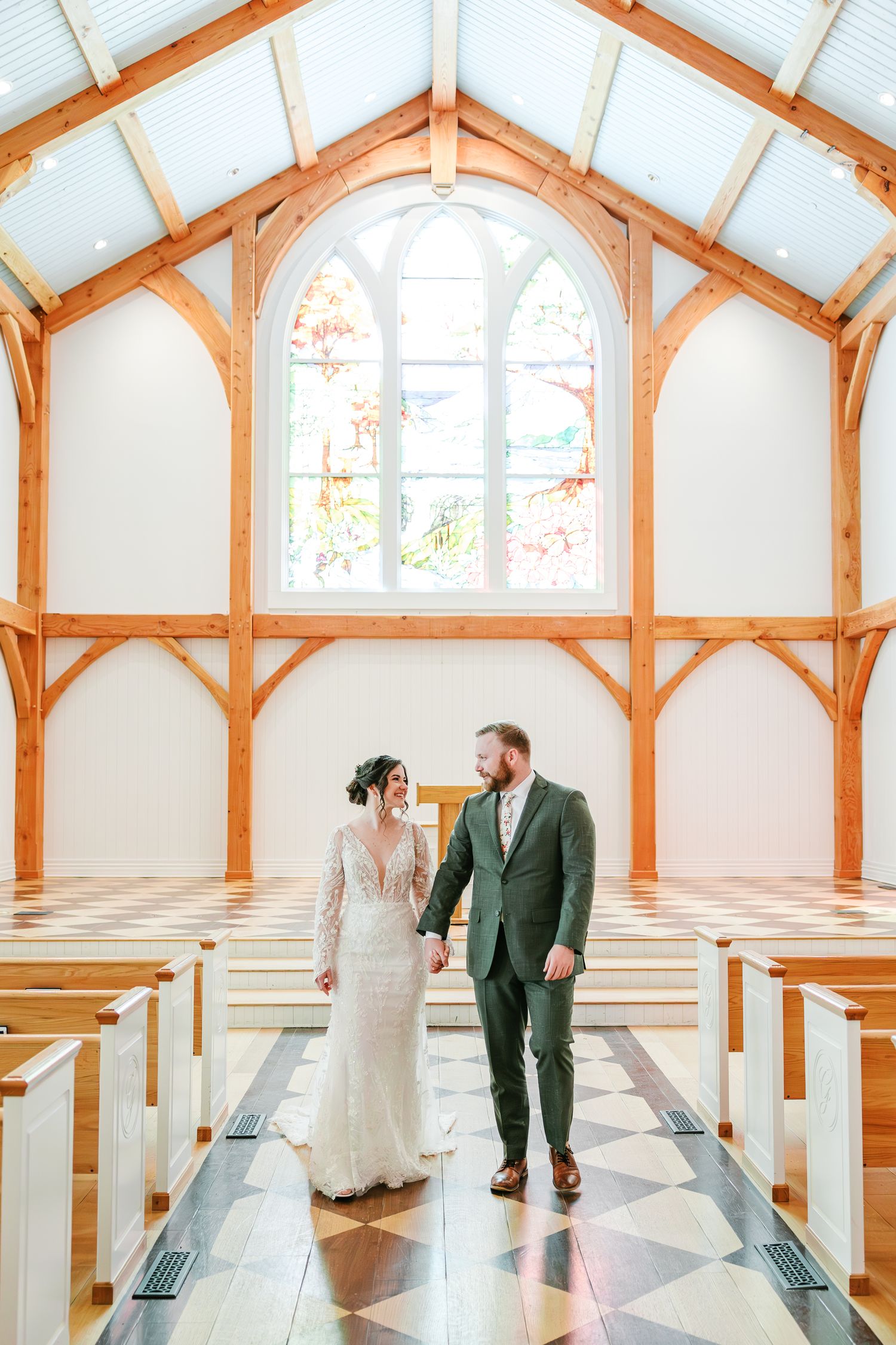 Wedding couple walking through bright chapel with wooden beams and white walls  with NC Wedding Photographer