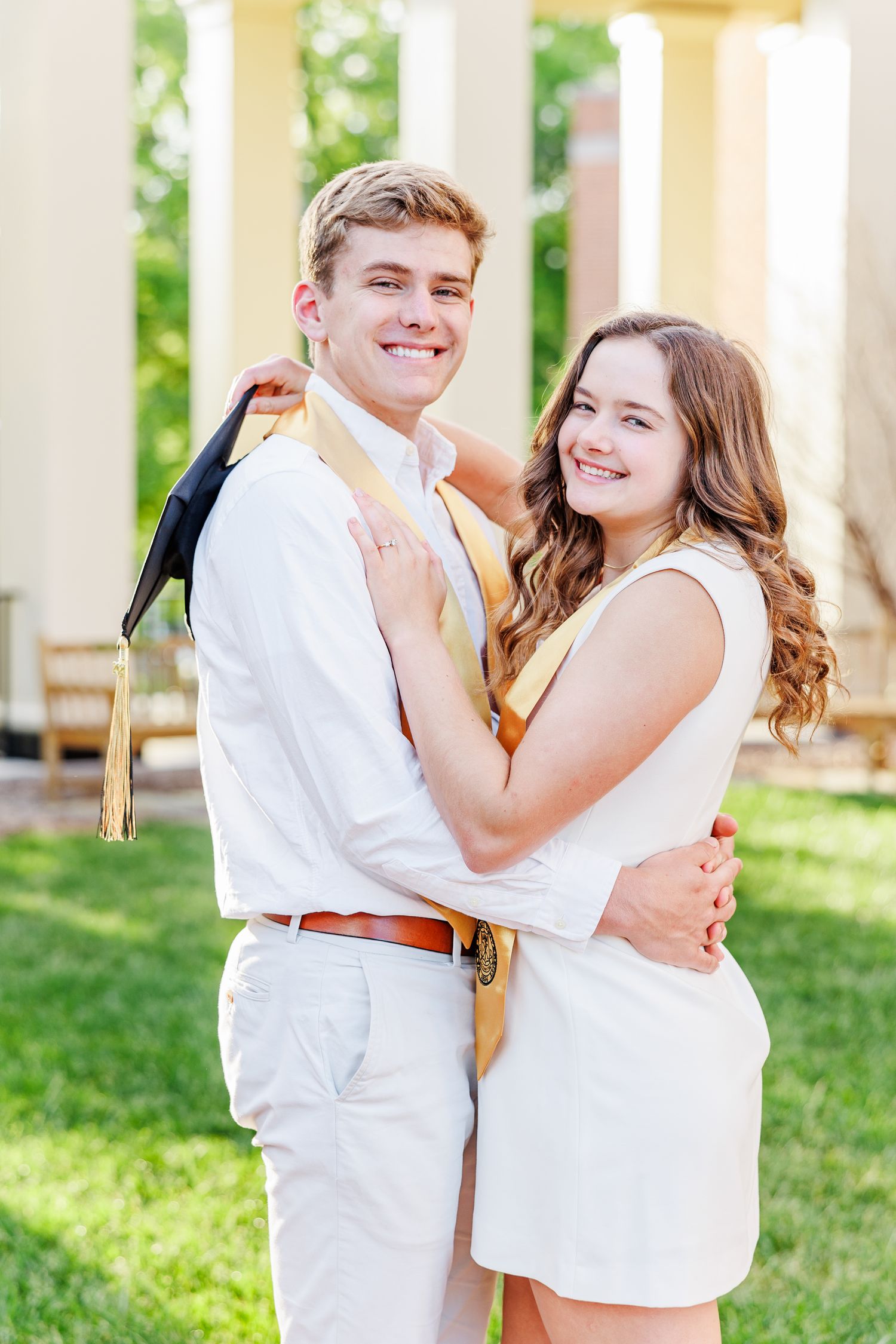 Couple in white outfits share playful moments under outdoor colonnade at Wake Forest University with a Graduation Photographer