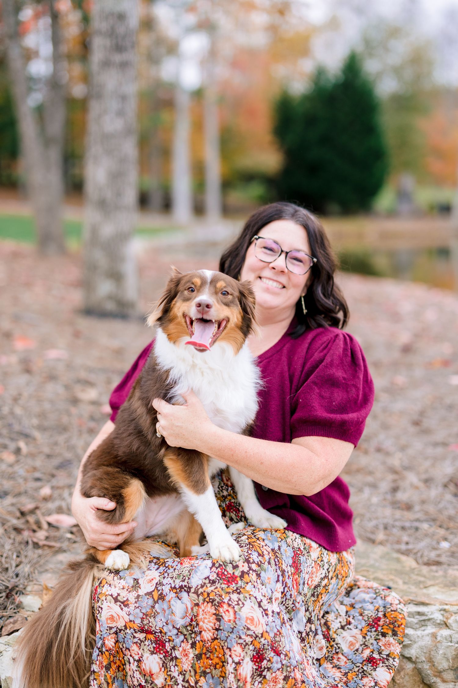 Person in purple shirt playing with a happy dog on fallen autumn leaves in Greensboro with a Family Photographer