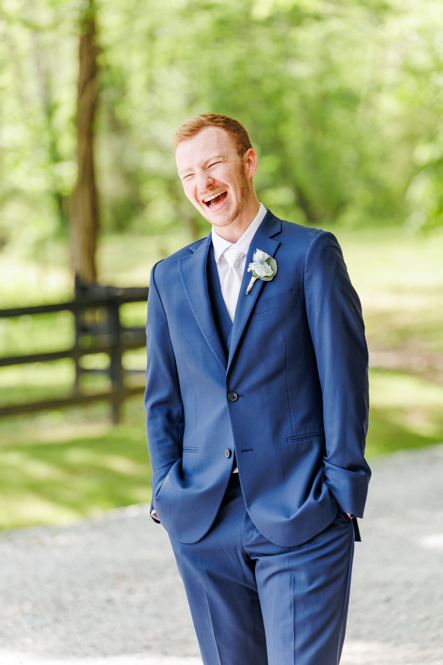 Groom in navy blue suit laughing during portrait session in a park setting with North Carolina Wedding Photographer
