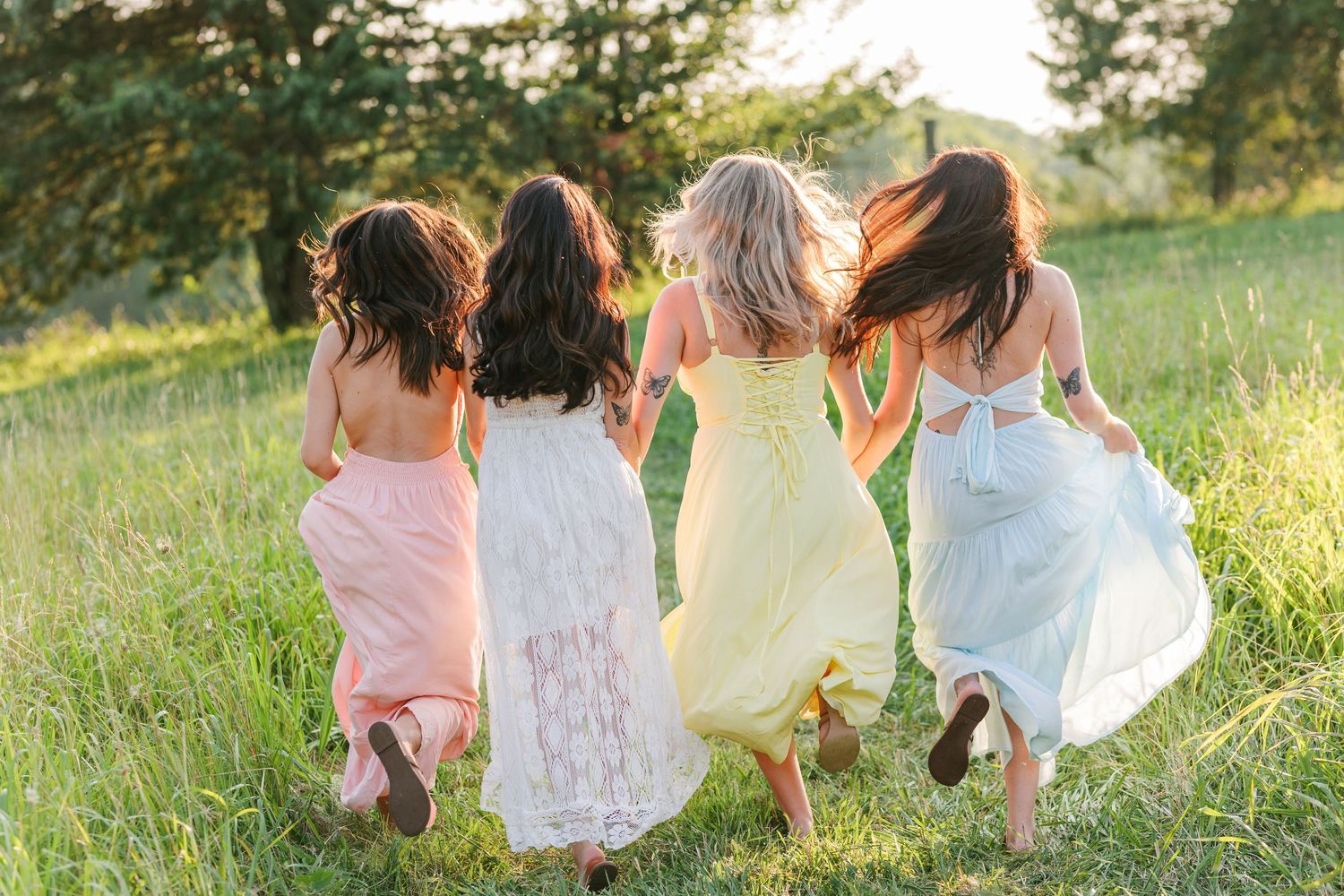 People in light colored dresses walk through a sun-drenched field during golden hour in Winston Salem with a Family Photographer