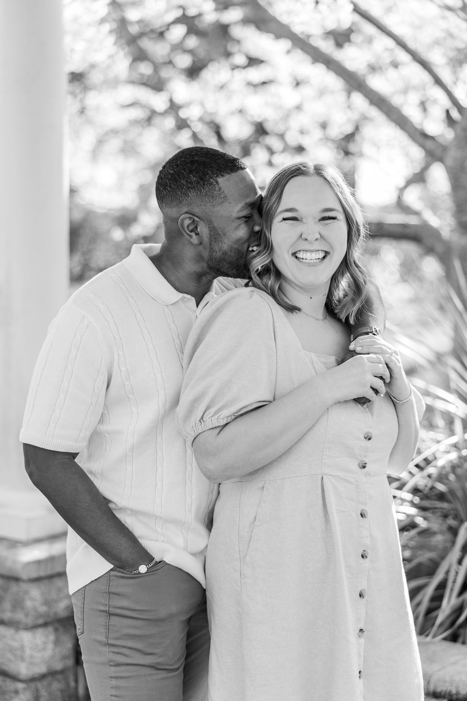 Black and white portrait of couple sharing tender moment under white columned porch Matthews NC Engagement Photographer