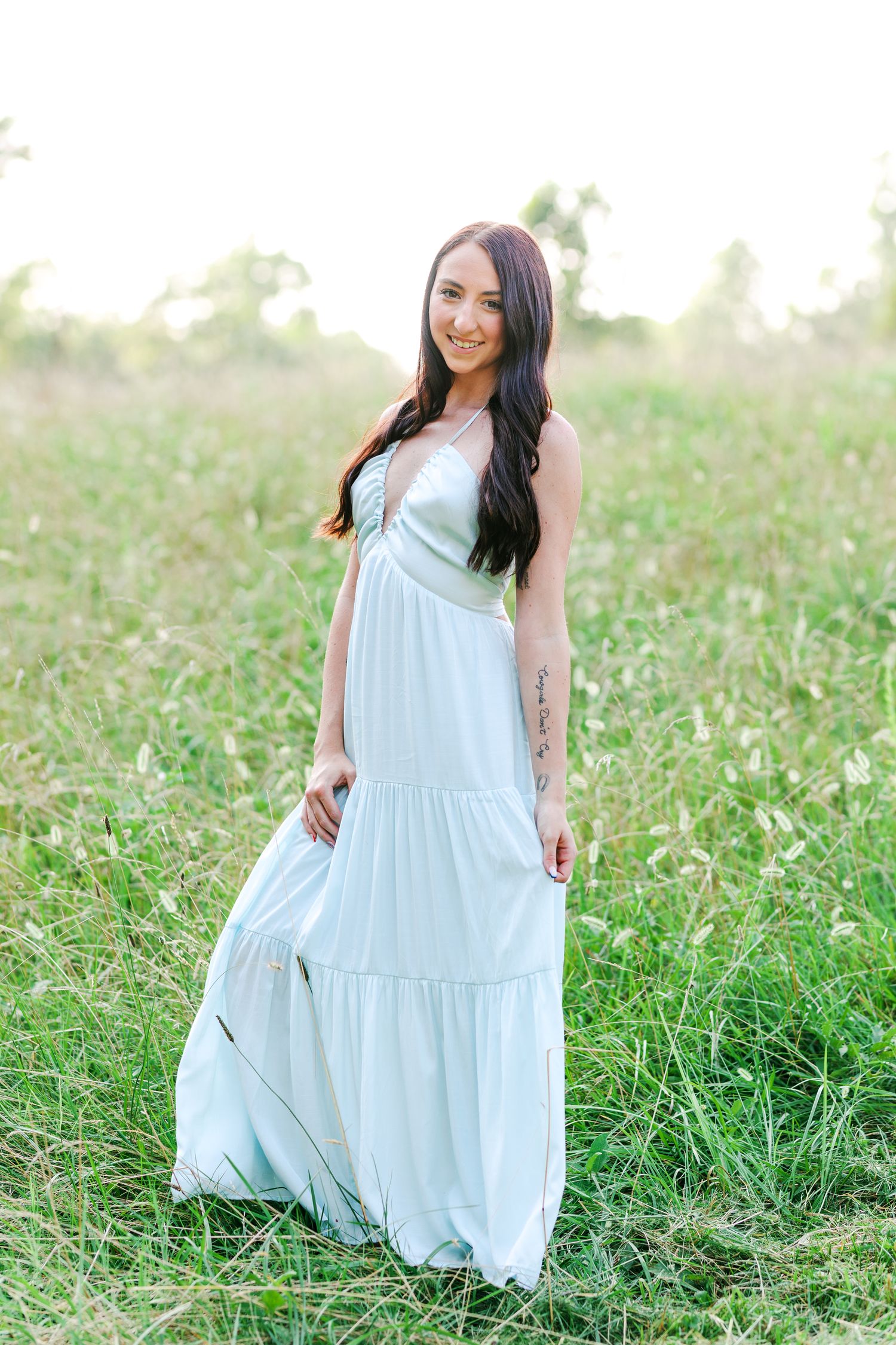 Person in a flowing light blue dress twirling in a sunlit field of wildflowers in Winston Salem with a Family Photographer