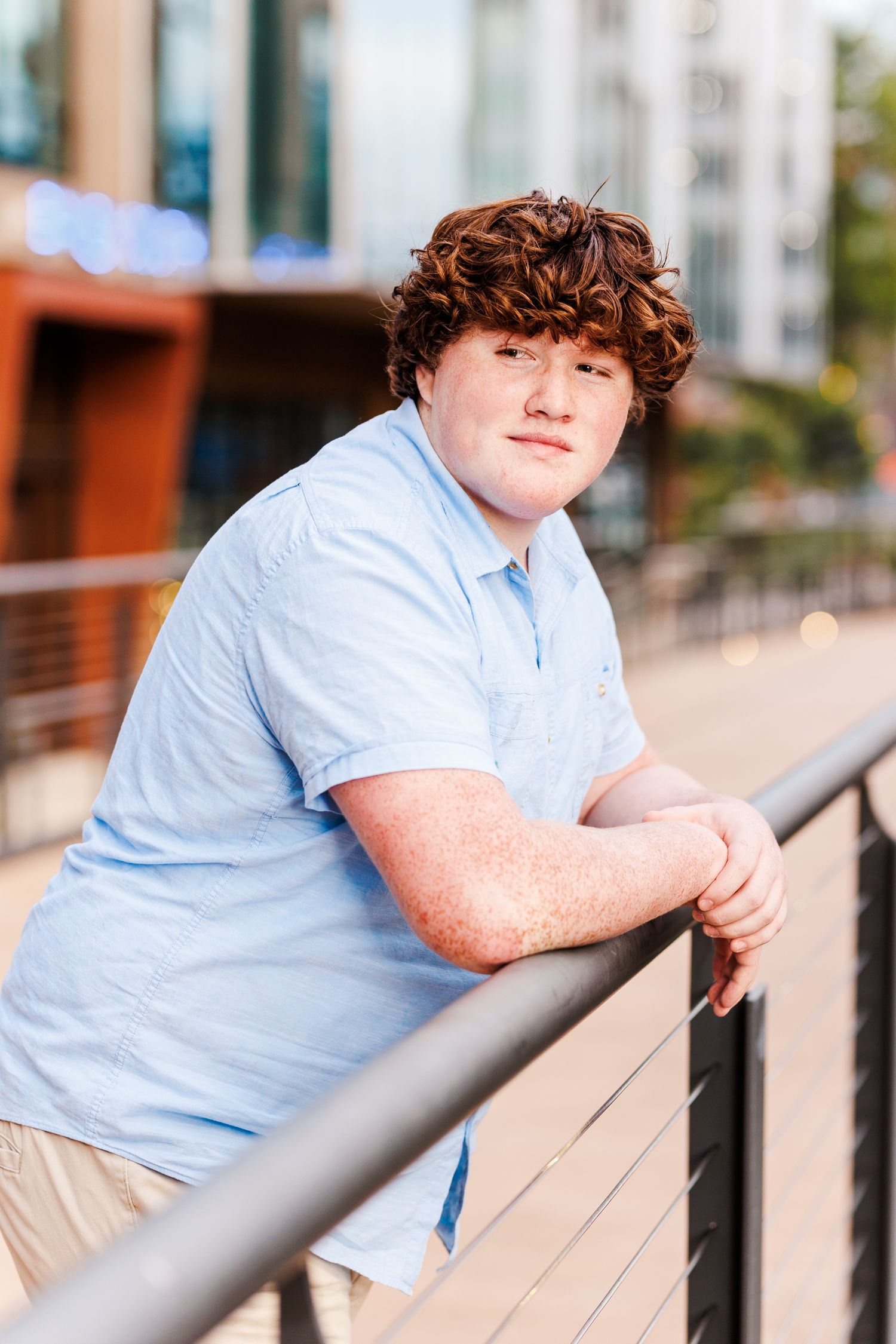Casual outdoor portraits leaning against metal railing in light blue shirt for Senior Portrait Session in Winston Salem