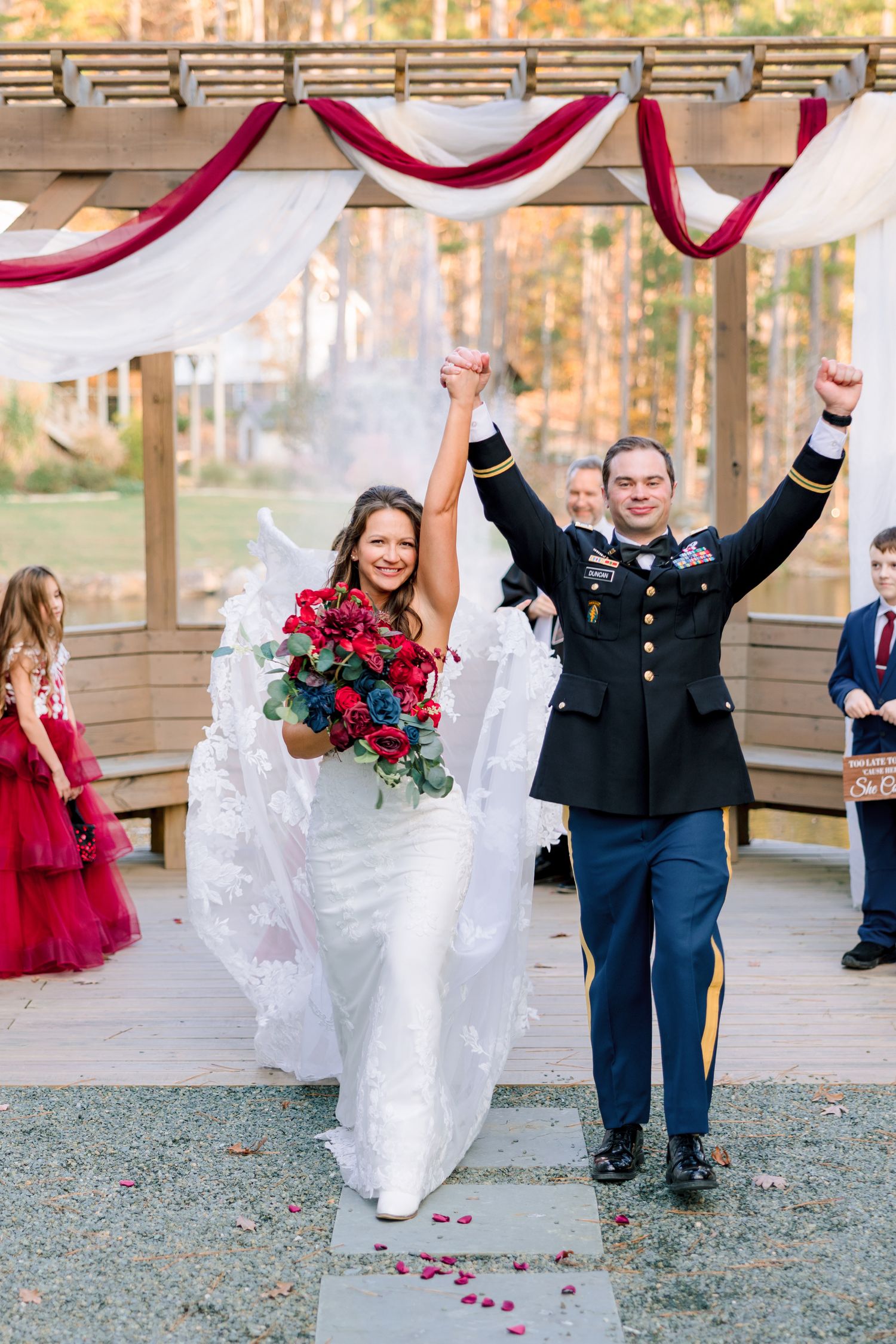 A joyful couple celebrates with raised arms under red and white wedding decor at the Barn at Union Grove Farm in Chapel Hill