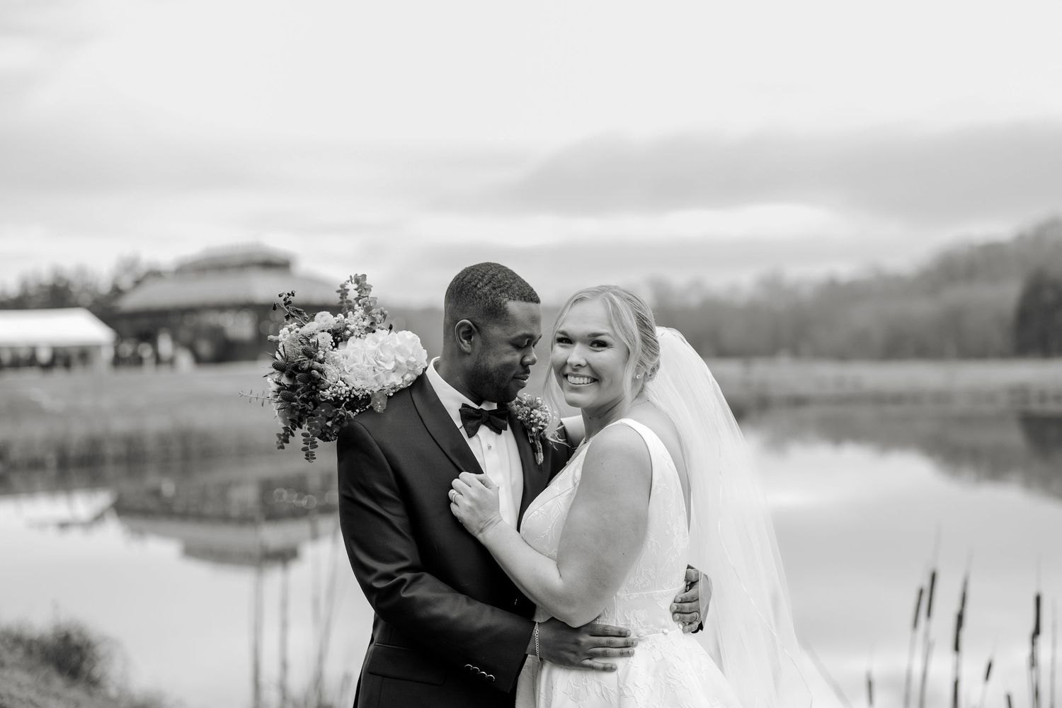 Black and white portrait of newlyweds embracing by serene lake.