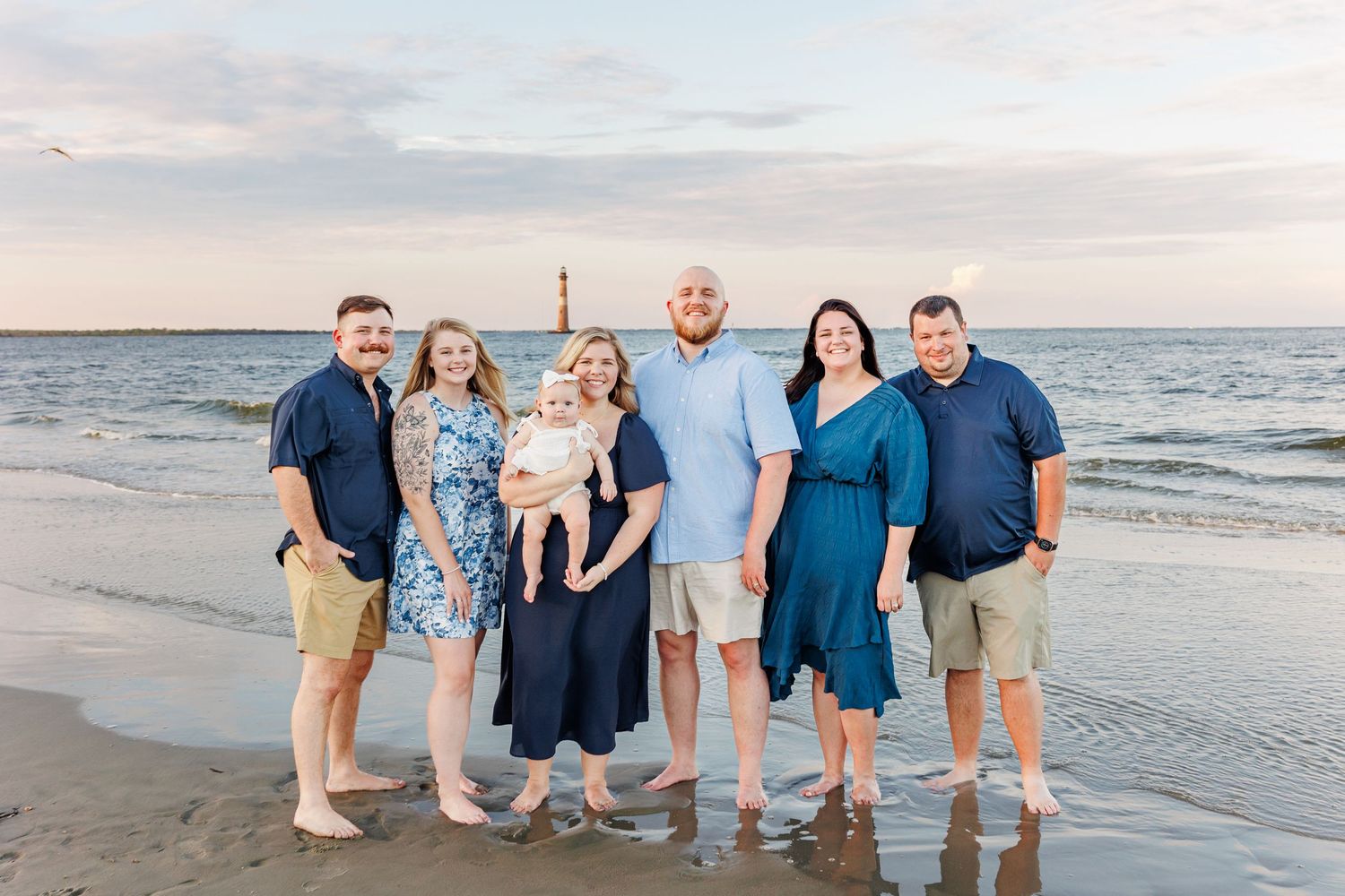 Extended family wearing coordinated blue and white outfits poses together on beach at sunset in Charleston with a SC Family Photographer
